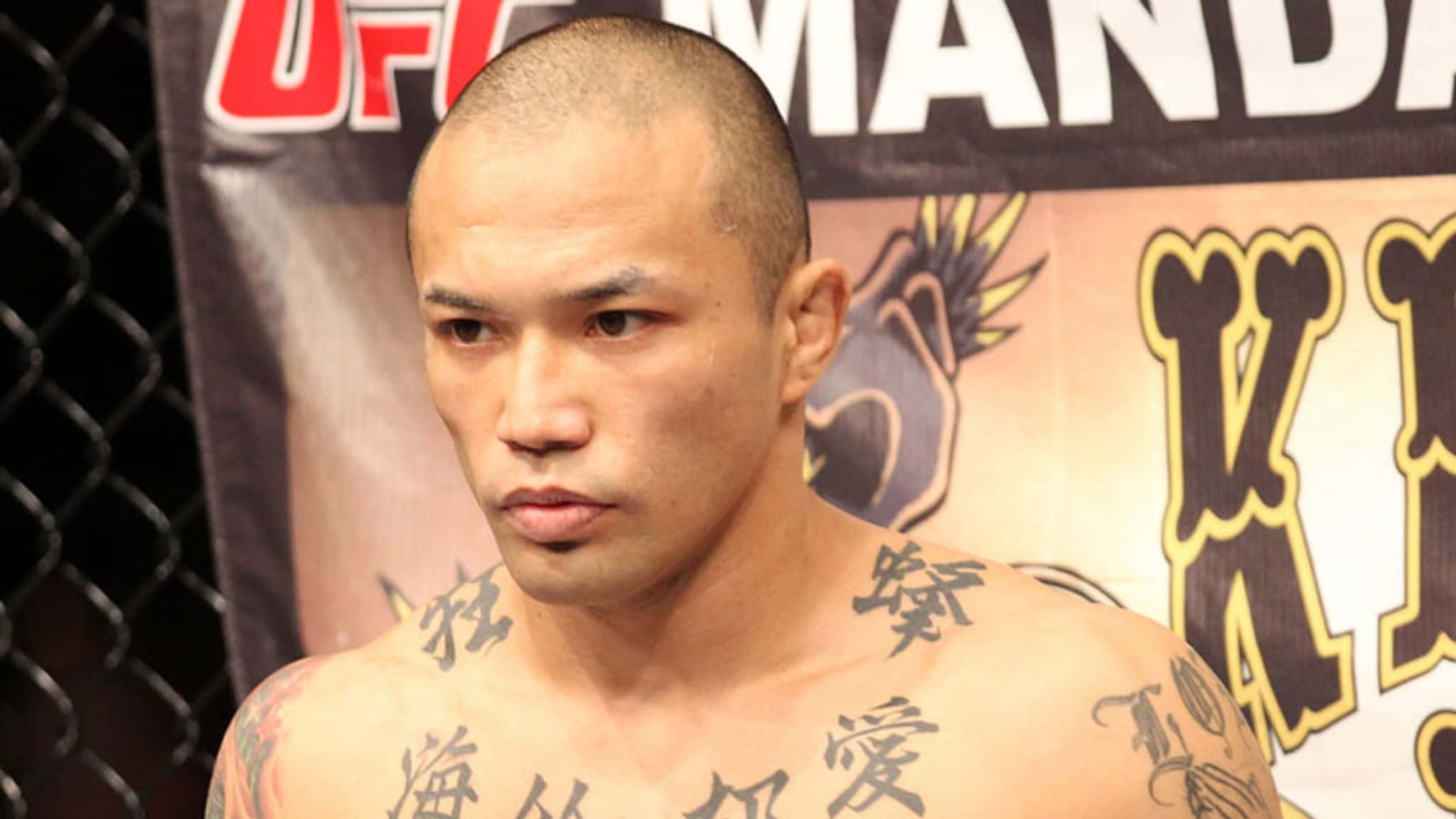 日本UFC選手山本信介2011年曼德勒灣活動中心賽事照 壁紙 — 一位專注的混合武術家，身上有紋身，在UFC八角籠內凝視著。