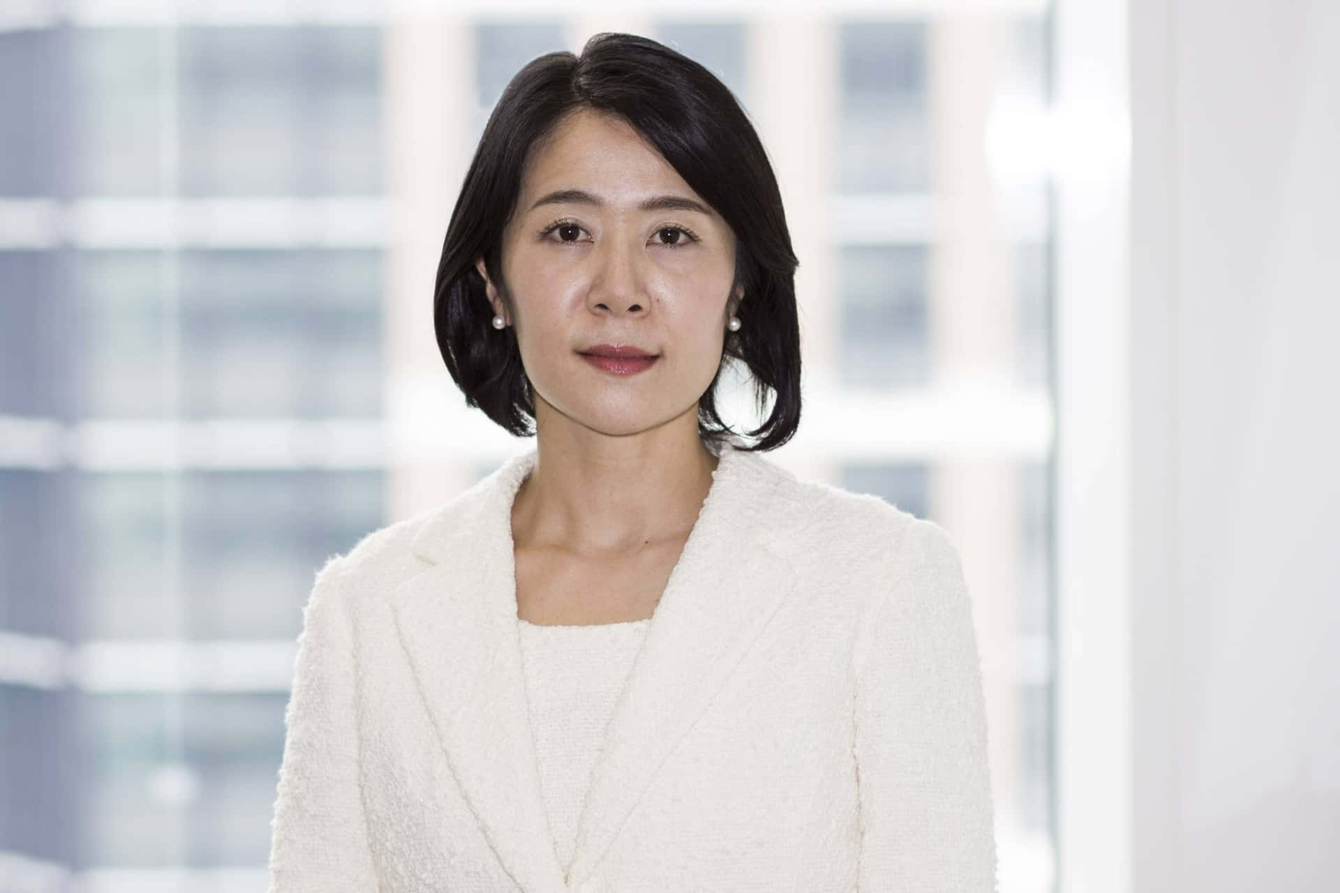 專業女性穿著白色西裝外套站在辦公室窗邊