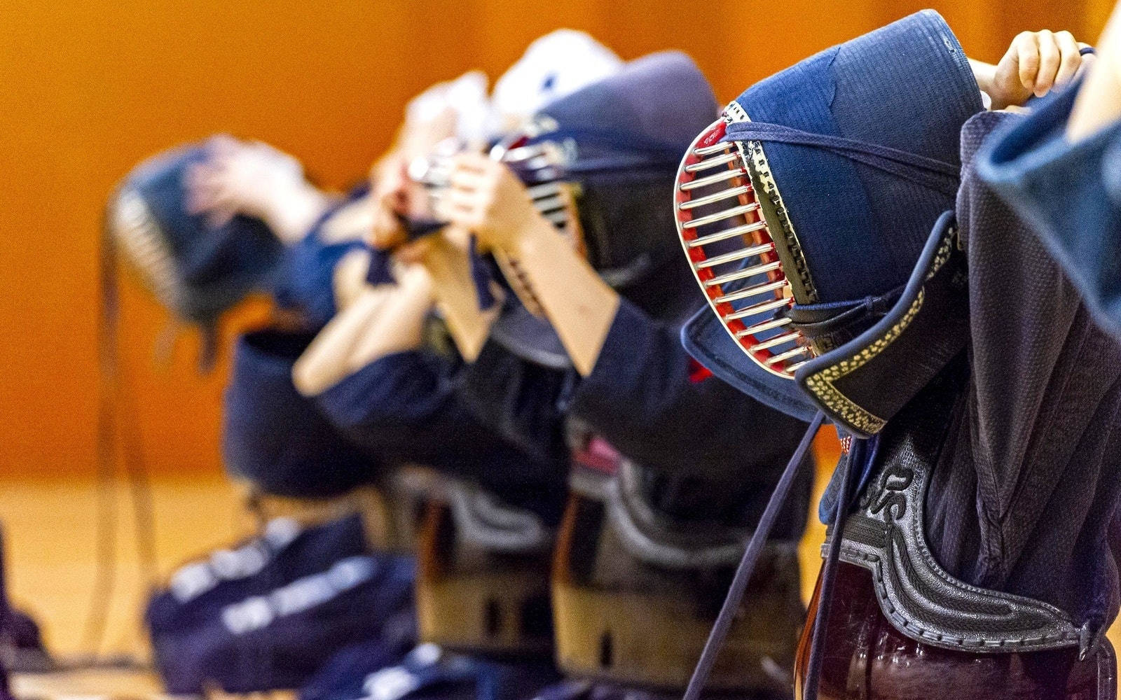 日本劍道武術 壁紙 — 一排身穿藍色制服和護具的劍道練習者坐在體育館內準備練習。