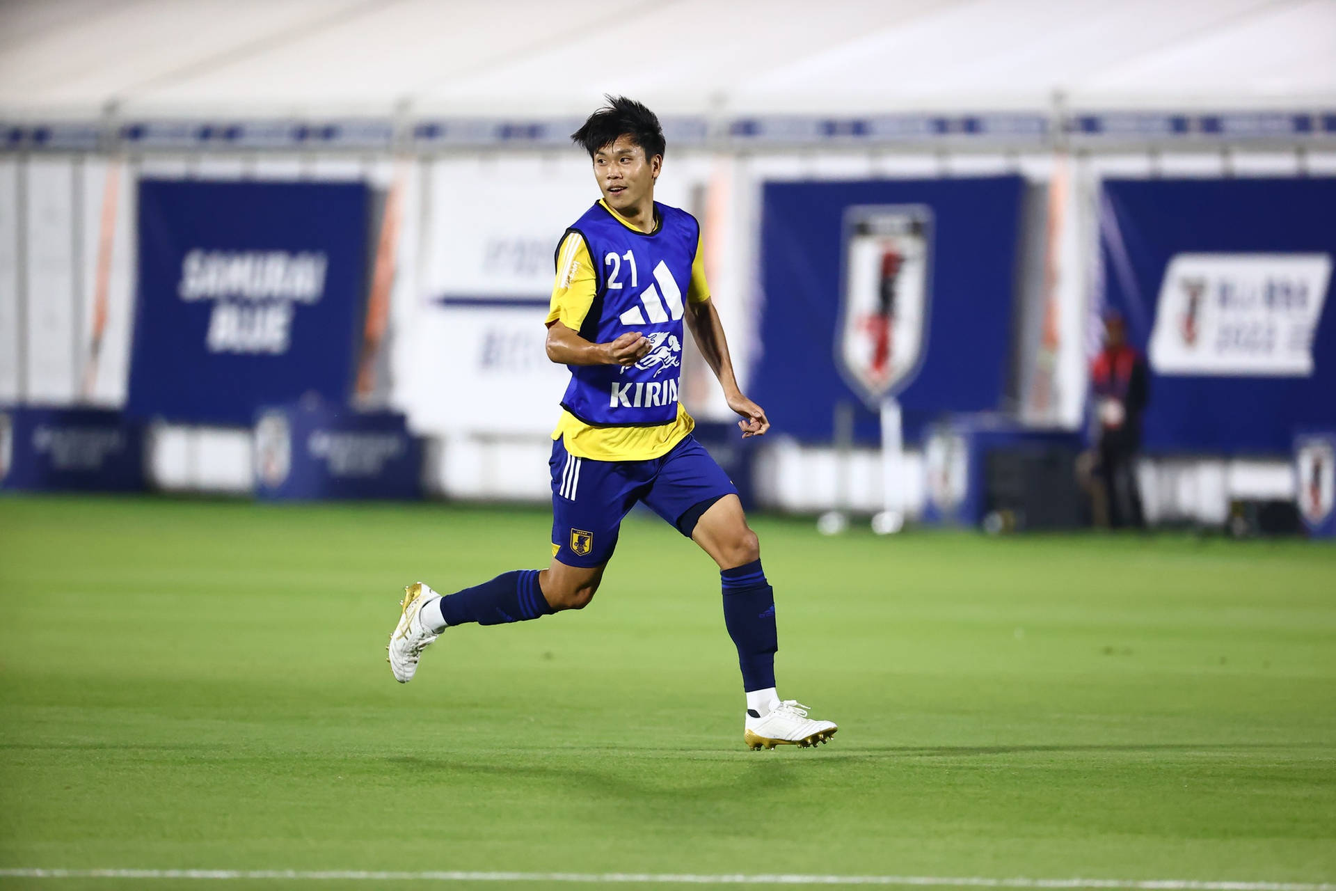 日本國家足球隊 前鋒上田绮世 壁紙 — 一名身穿藍黃球衣的足球員在球場燈光下於翠綠草地上飛奔。