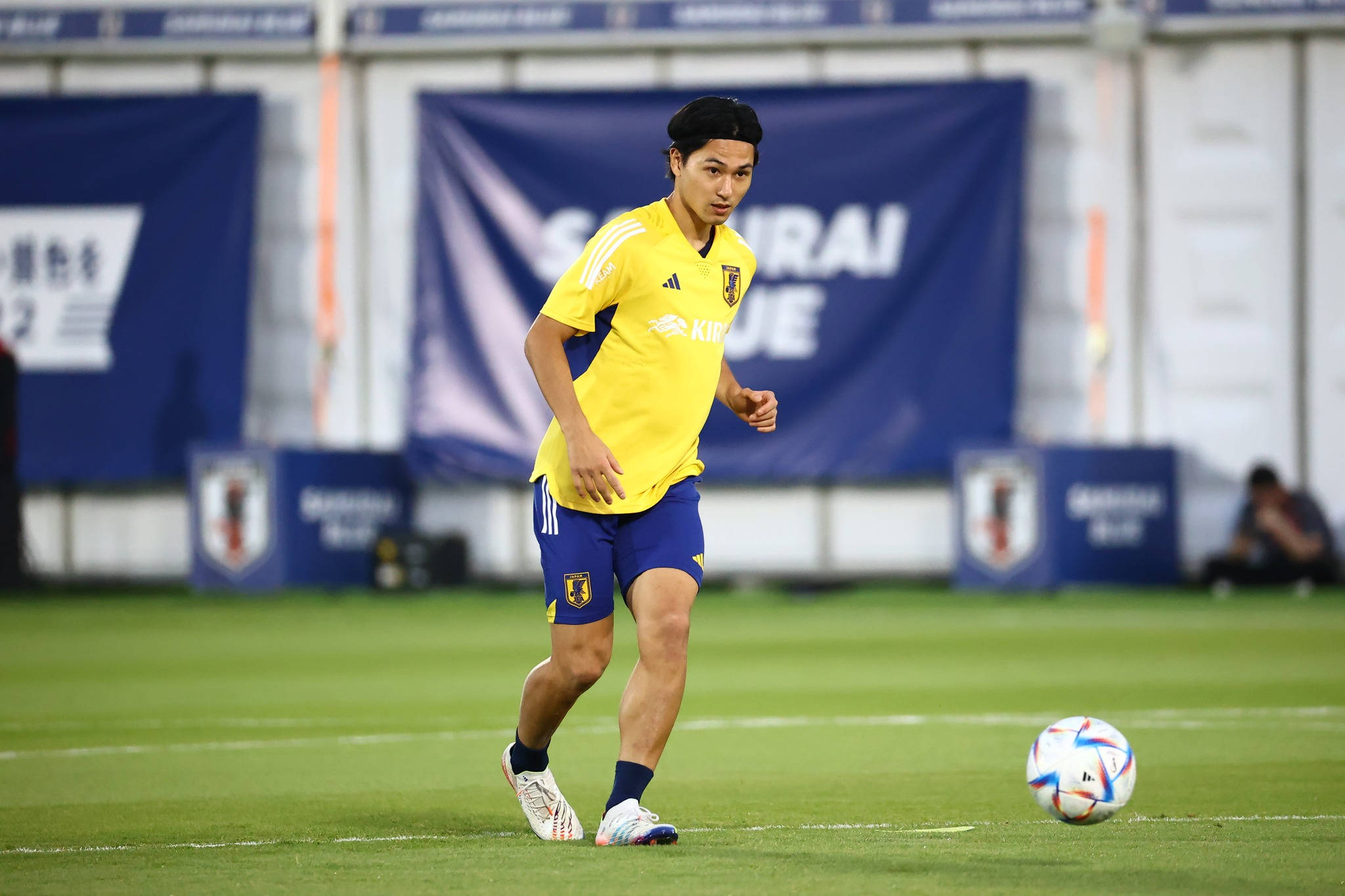 日本國家足球隊濱田暖身 壁紙 — 一名身穿黃藍色球衣的日本足球員，在球場燈光下的綠色草地上盤球。