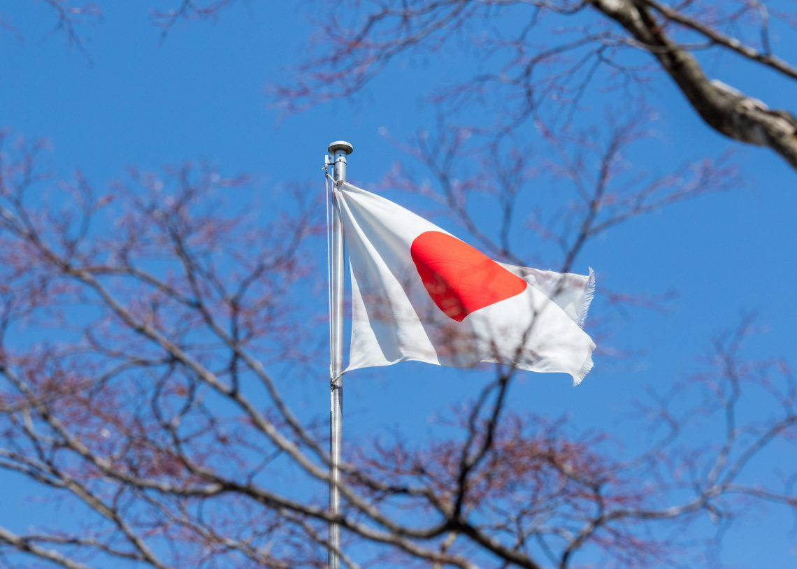 日本國旗與藍天景色 壁紙 — 日本國旗，紅色圓形波浪在清澈藍天下，由光禿樹枝框住。