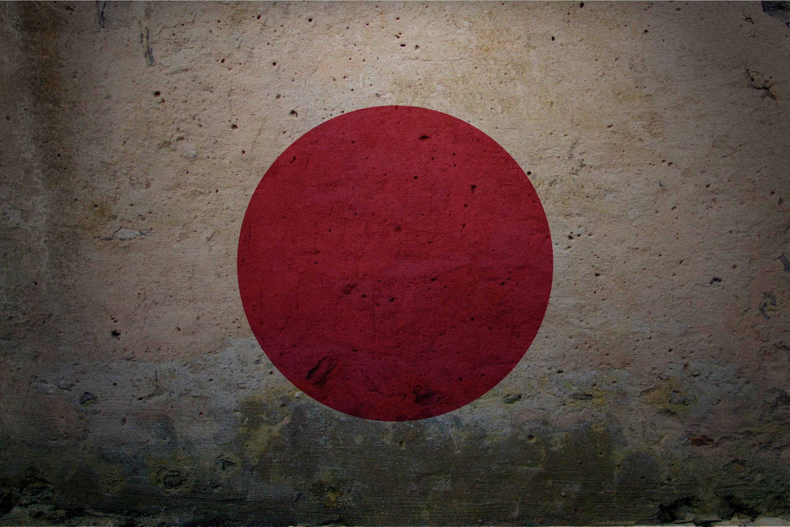 日本國旗貼於舊牆 壁紙 — 一幅褪色的日本國旗繪在裂開的混凝土牆上，帶有粗糙紋理和褪色的紅色圓圈。