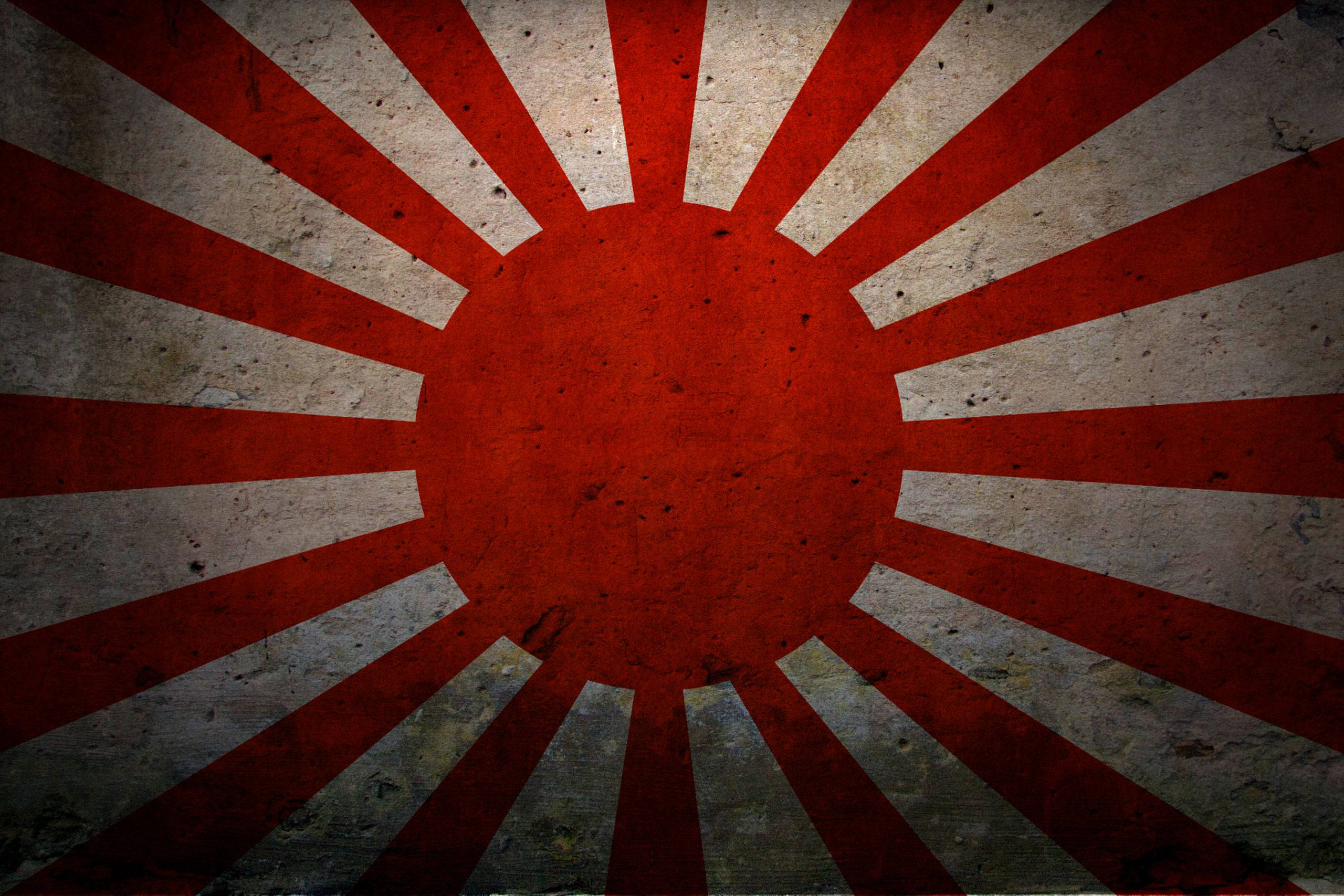 日本國旗貼於髒污牆壁 壁紙 — 一面風化的日本旭日旗，紅色光線在帶紋理的灰色背景上。