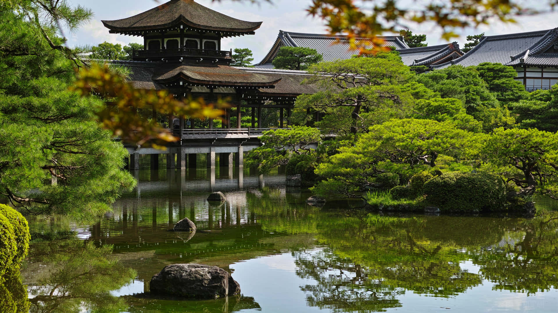 日本寺廟亭閣倒映在平靜的池塘中，周圍有綠樹。