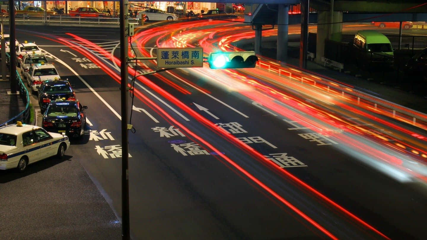 日本夜間道路背景 壁紙 — 長時間曝光捕捉到夜間繁忙東京高速公路上紅色尾燈和白色頭燈的流動痕跡。