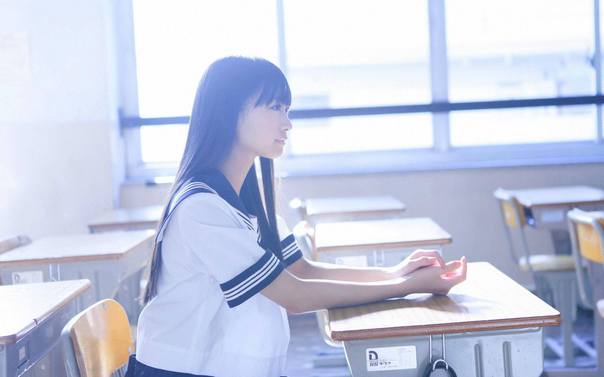 一位穿著水手服嘅學生坐在空課室嘅書枱，望住窗戶。