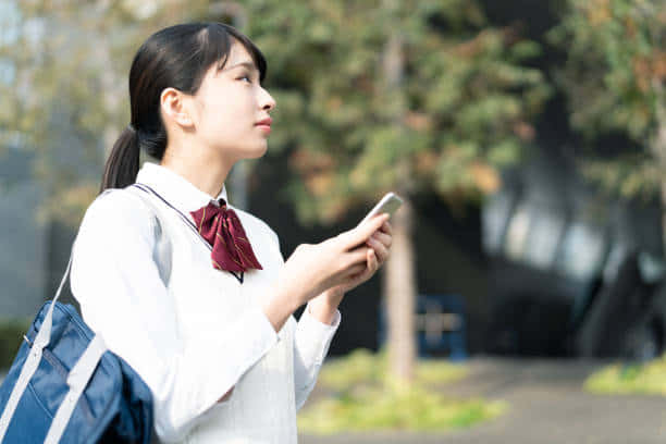 一名穿著校服的年輕學生在戶外拿著手機。