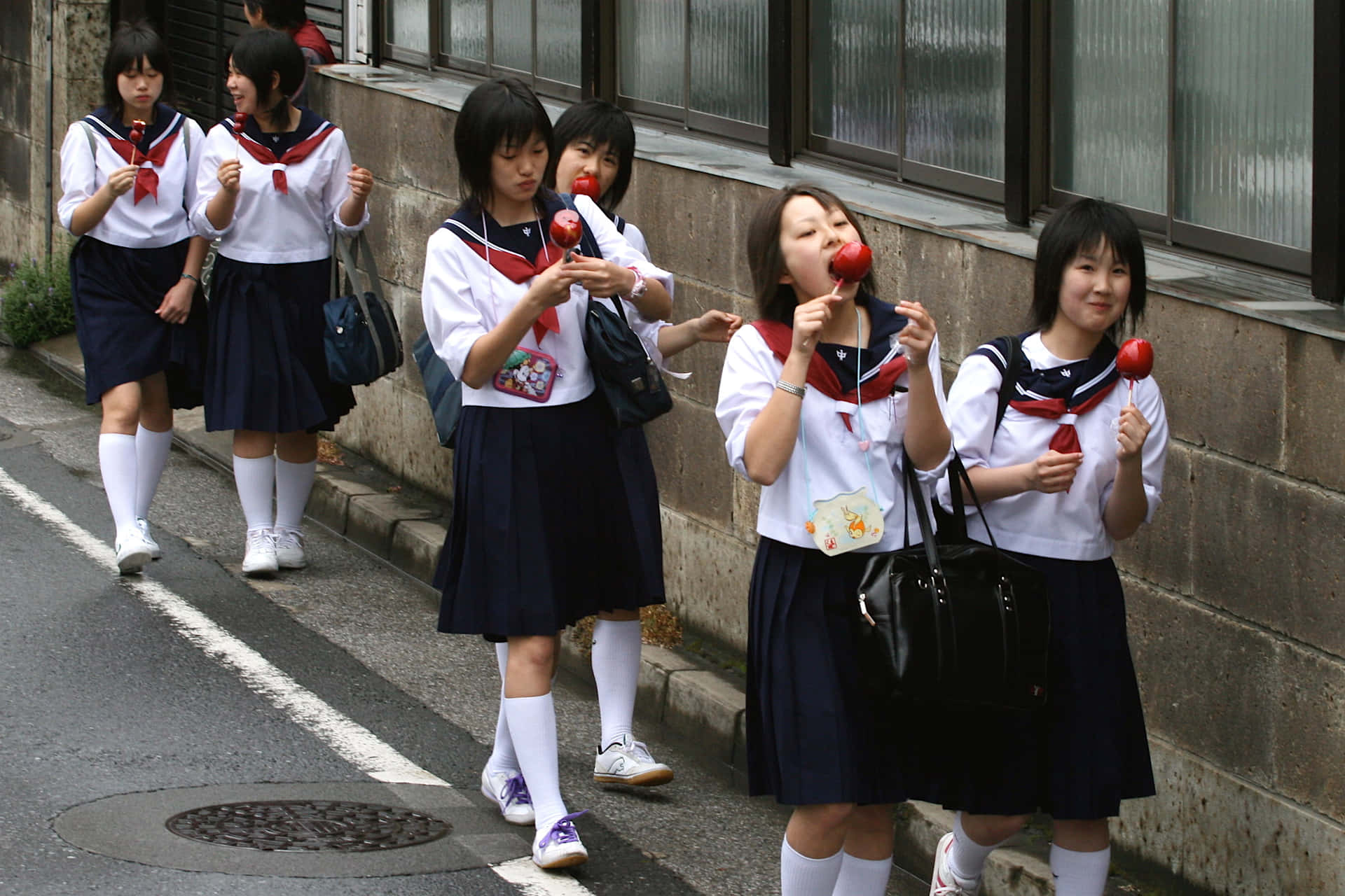 日本女學生在城市人行道上吃紅蘋果棒棒糖。