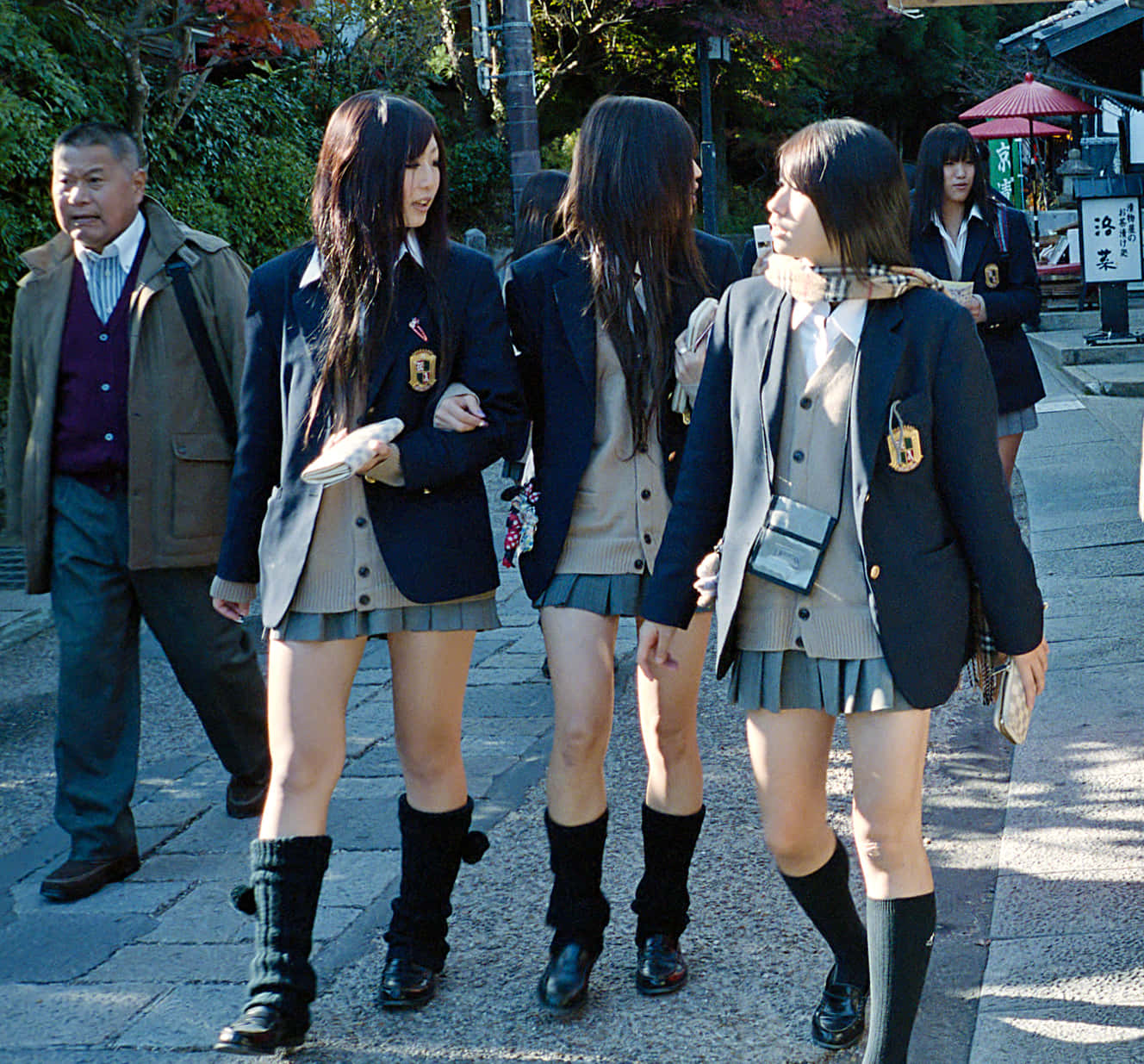 三名身穿校服的日本女學生在陽光明媚的秋日街道上行走。