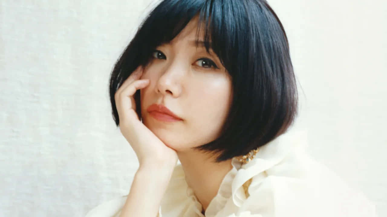 短黑髮女性在柔和燈光的攝影棚肖像中將下巴擱在手上。