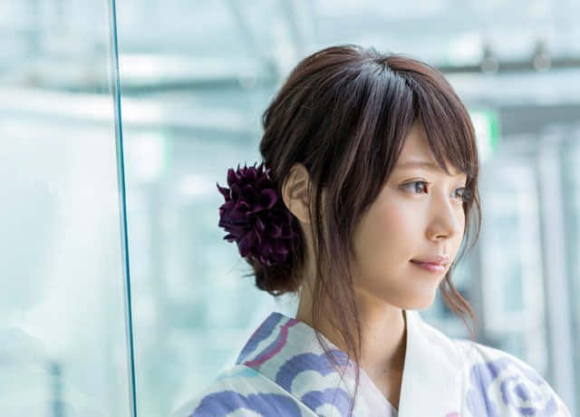 年輕女子身穿浴衣，頭髮上插著紫色花朵，望著窗外