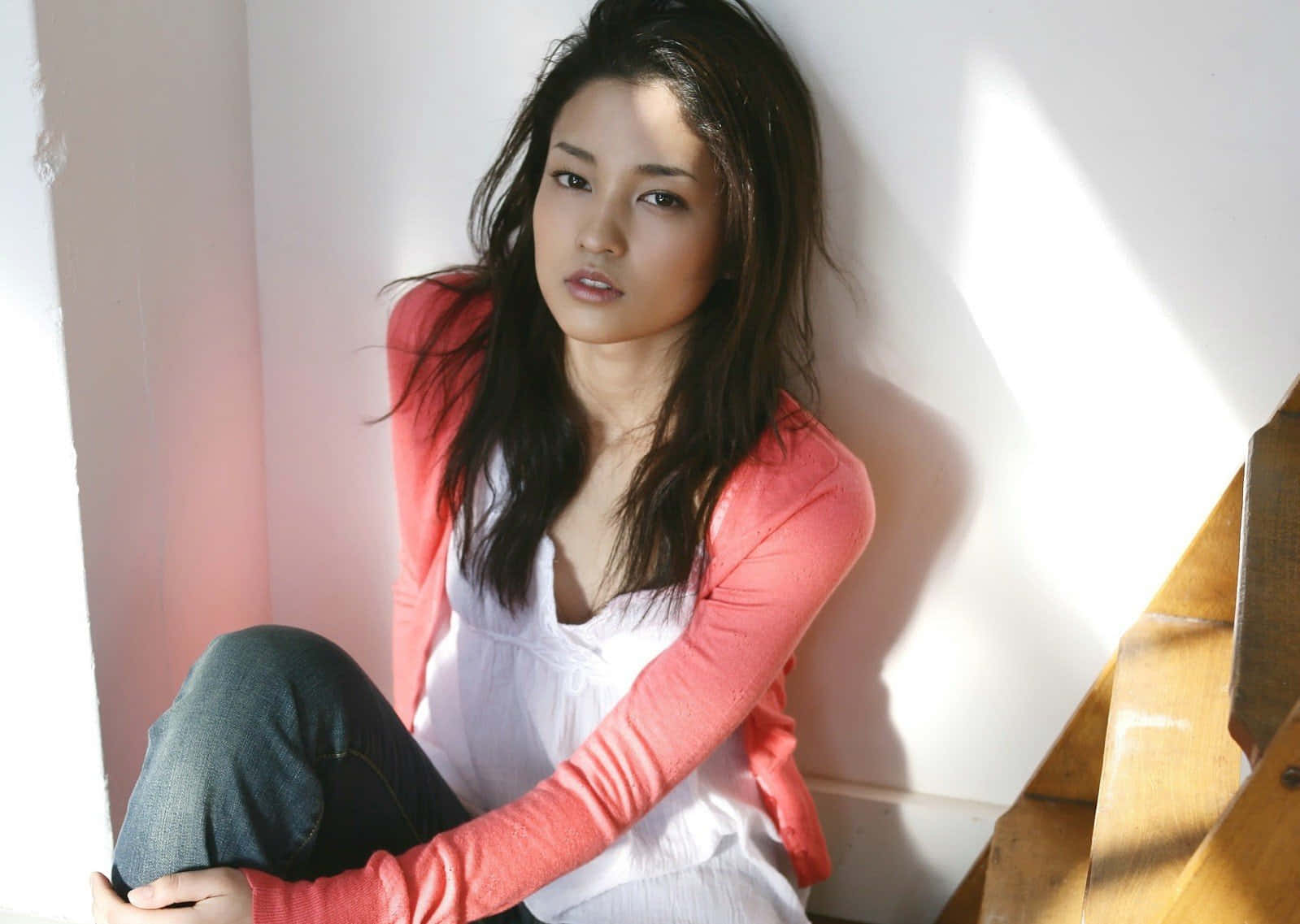 年輕女性在室內柔和陽光下坐在木樓梯上。
