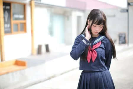 年輕女孩穿著水手服站在街上，手靠近耳朵。