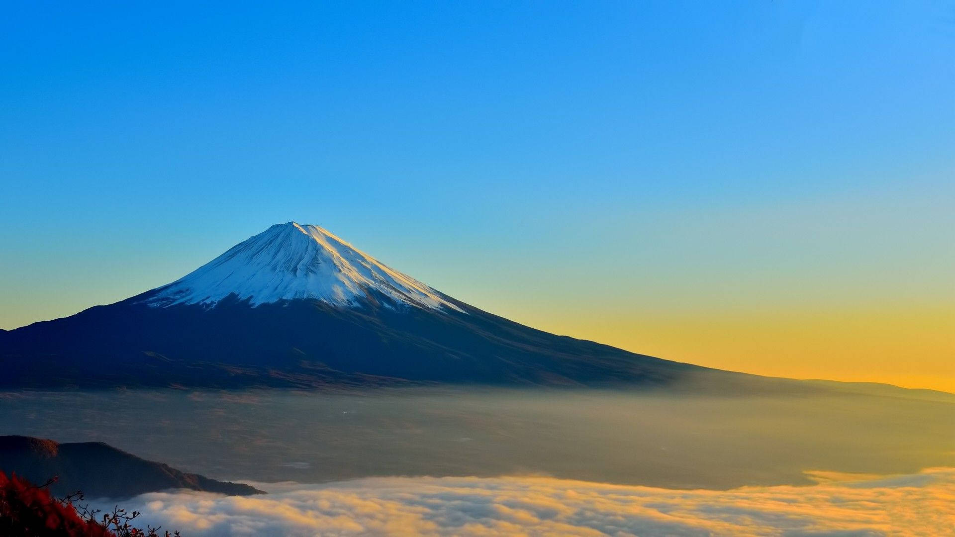 日本富士山秋日壯麗風景 壁紙 — 白雪覆蓋的富士山在晴朗的藍天下，於日出時分雄偉地聳立在金色雲海之上。