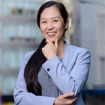 一位身穿藍色西裝外套的自信女性，在城市戶外擺姿勢時微笑。