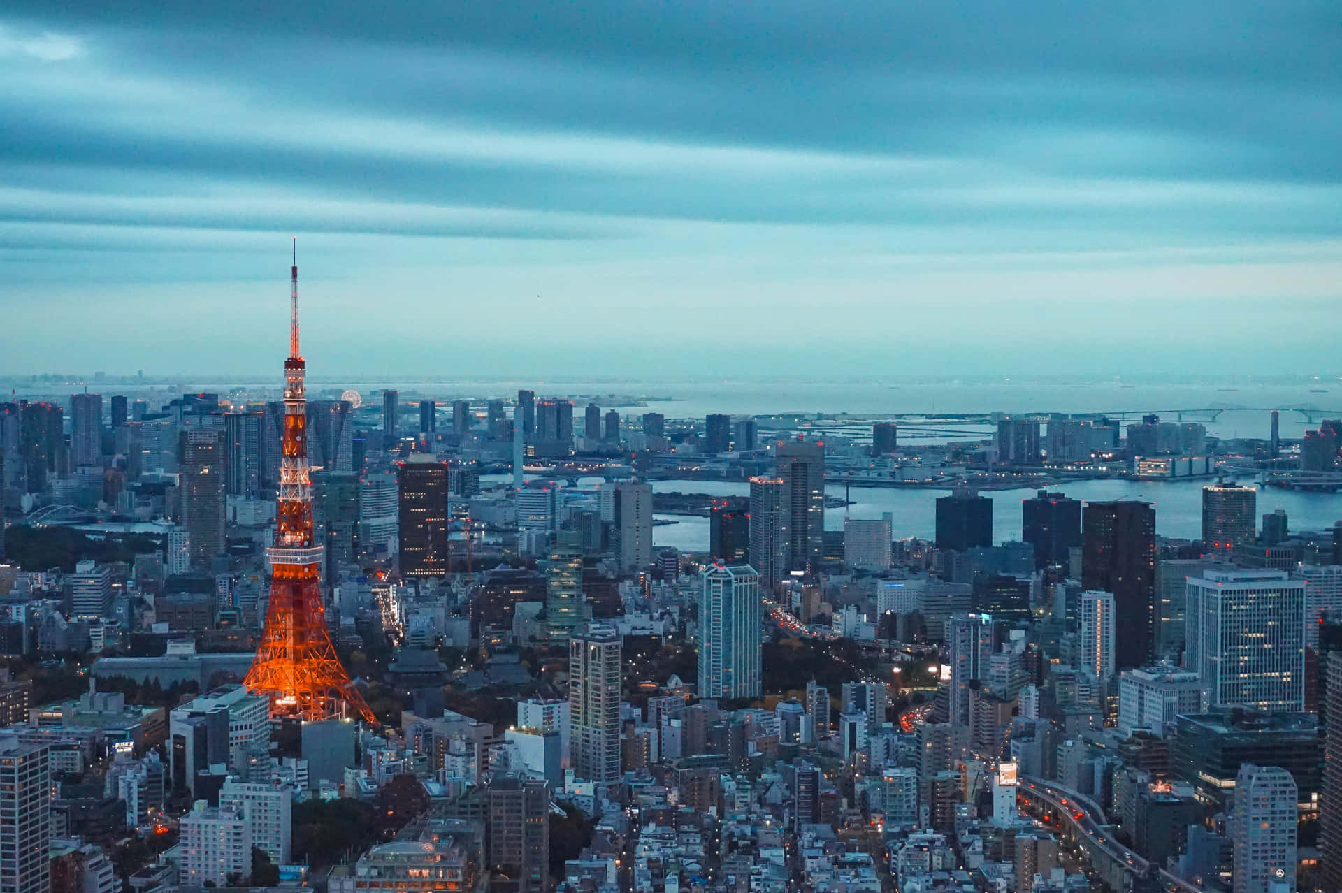 日本東京城市全景 壁紙 — 東京塔在昏暗的藍天下溫暖地發光，城市燈光在都市擴展區閃爍。