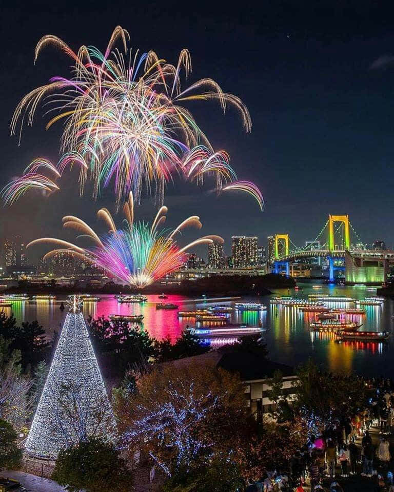 日本東京灣的壯麗彩虹橋景觀 壁紙 — 色彩繽紛的煙花在東京彩虹橋上空綻放，船隻在水面反射的耀眼燈光下滑行。