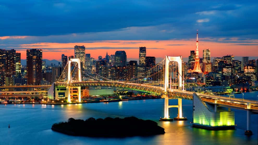 日本東京的壯麗彩虹橋 壁紙 — 彩虹橋在黃昏時分在東京灣上空閃耀，東京塔在火紅橙色和深藍色的天空下亮起。
