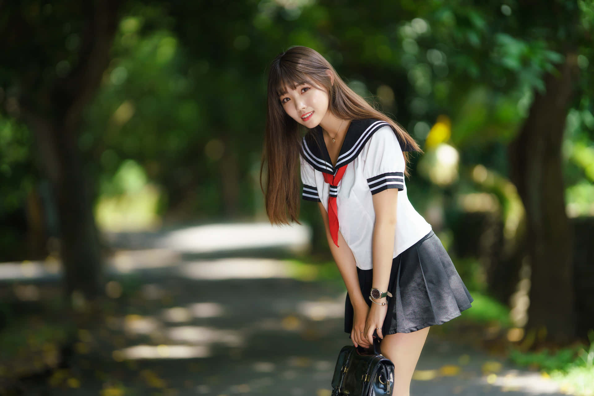 一個穿著校服的女孩在公園裡拿著袋子微笑著靠著。