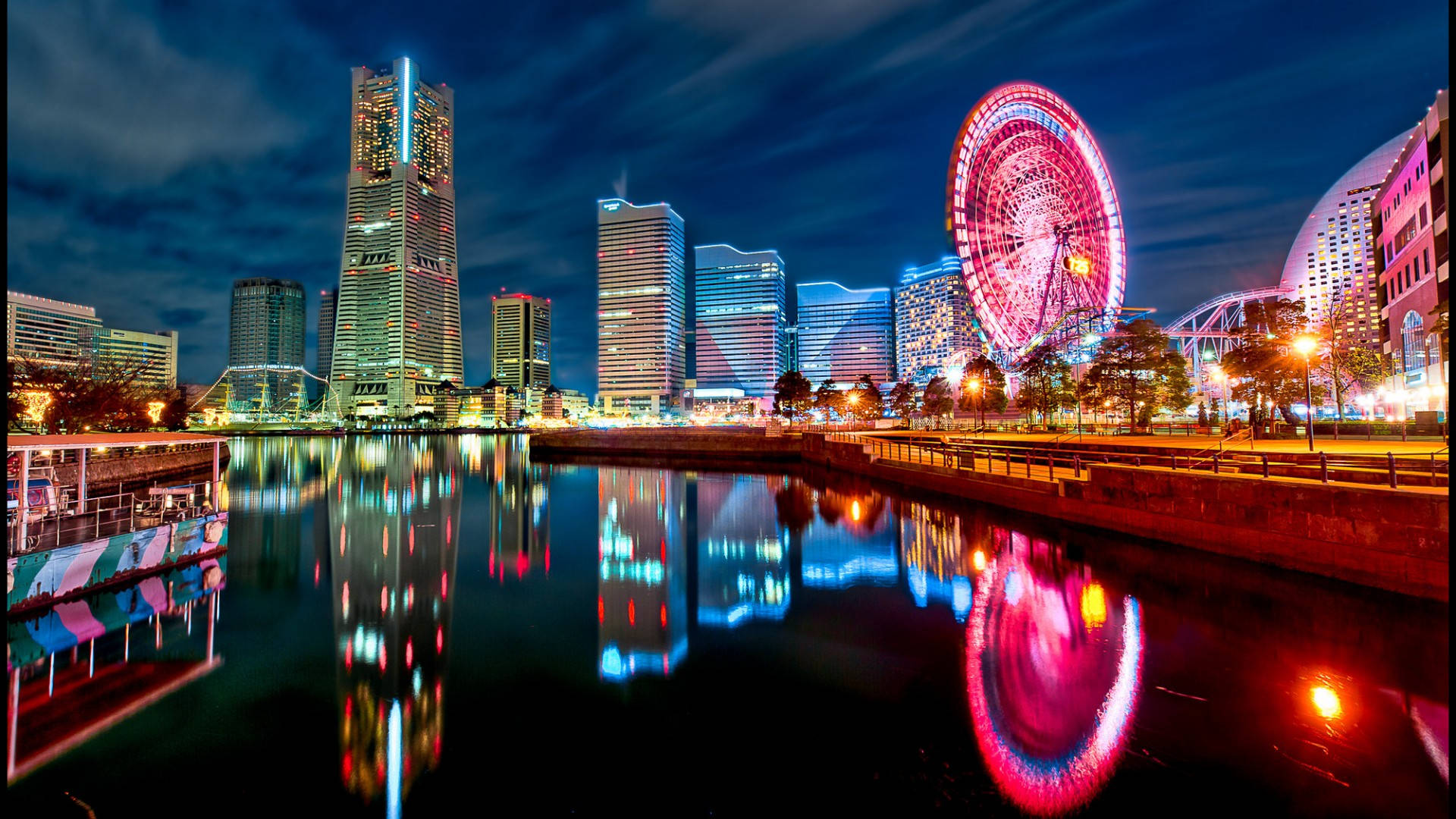 日本橫濱城市夜景 壁紙 — 充滿活力的夜景城市景觀，閃爍的摩天大樓和色彩繽紛的摩天輪倒映在平靜的水面上。