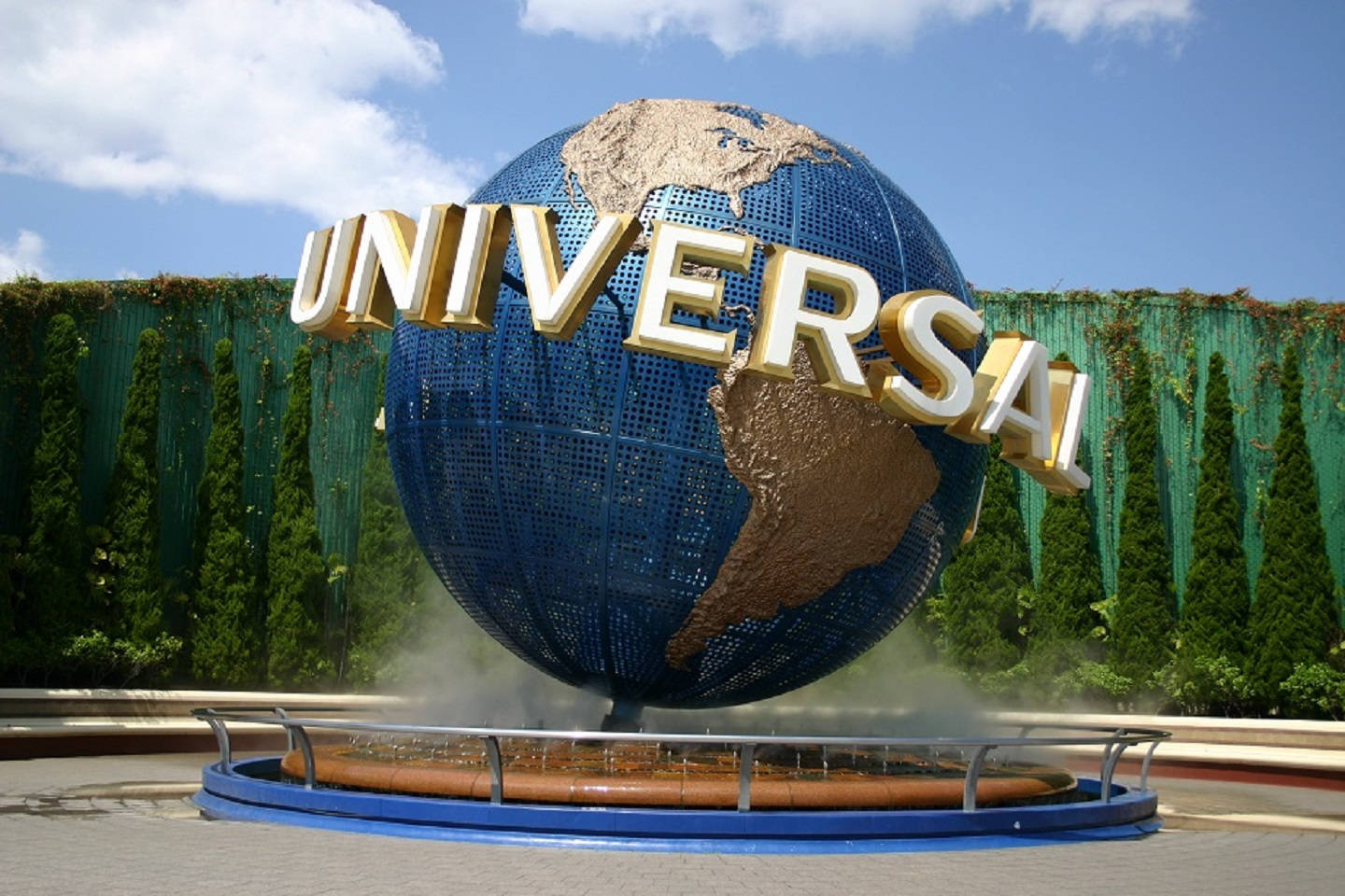 日本環球影城地球儀 壁紙 — 一個巨大的藍色地球儀，上面有金色的「UNIVERSAL」字母，拱形跨越噴泉，背景是晴朗的藍天和蓬鬆的白雲。