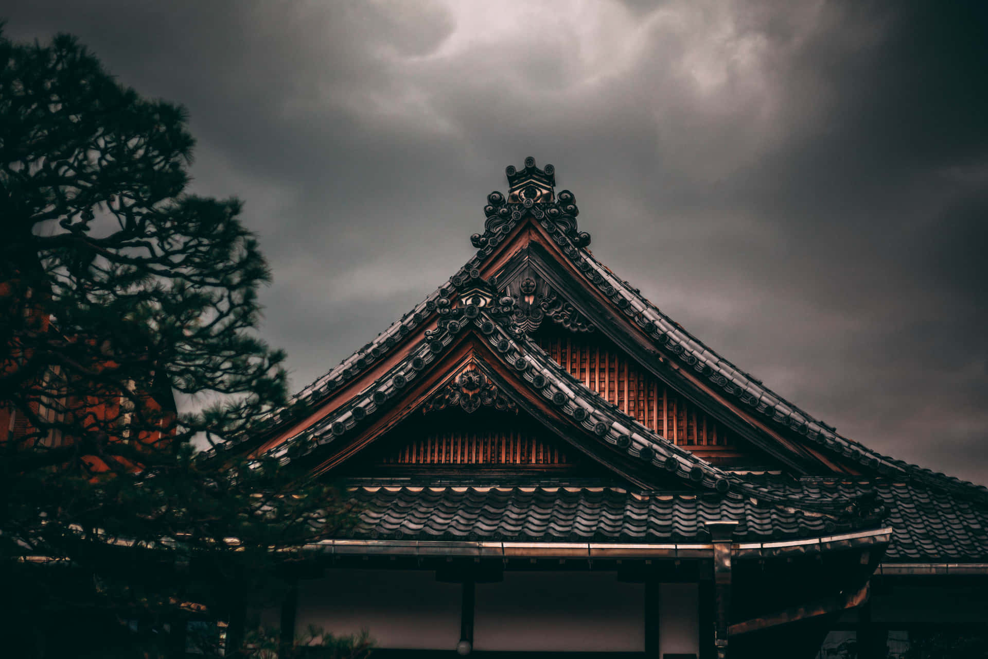 陰沉暴風雨天空下帶有松樹剪影的深色傳統日本寺廟屋頂。