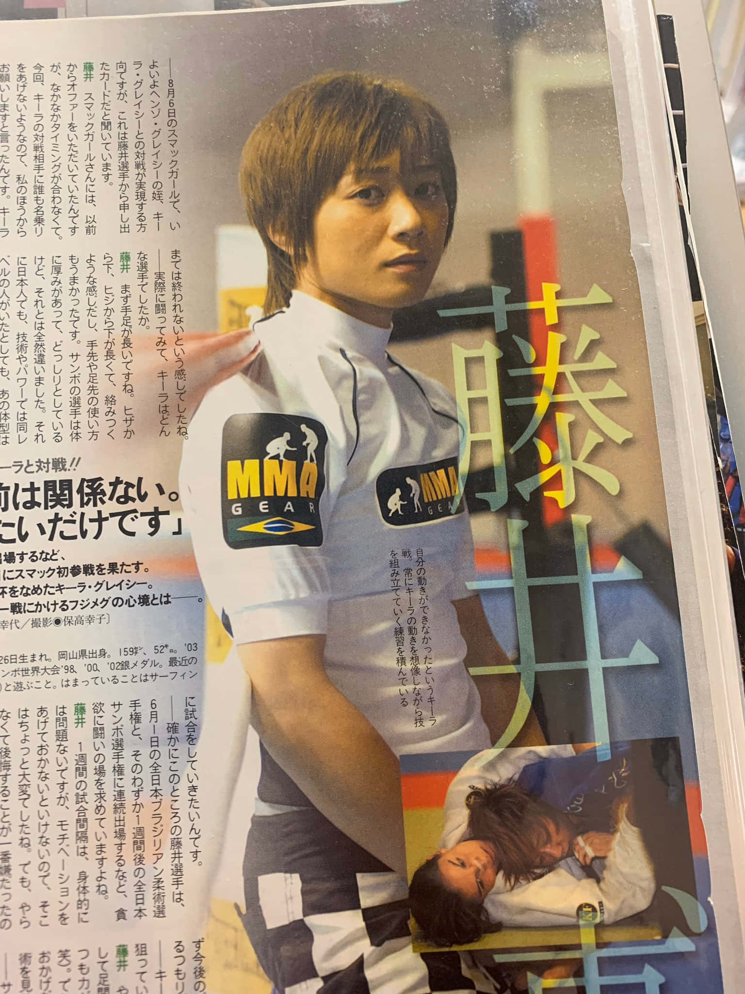 日本綜合格鬥選手梅古美·藤井新聞專題 壁紙 — 一位身穿白色制服的日本MMA拳手在雜誌版面中自信地擺姿勢，版面包含粗體漢字和動作照片。