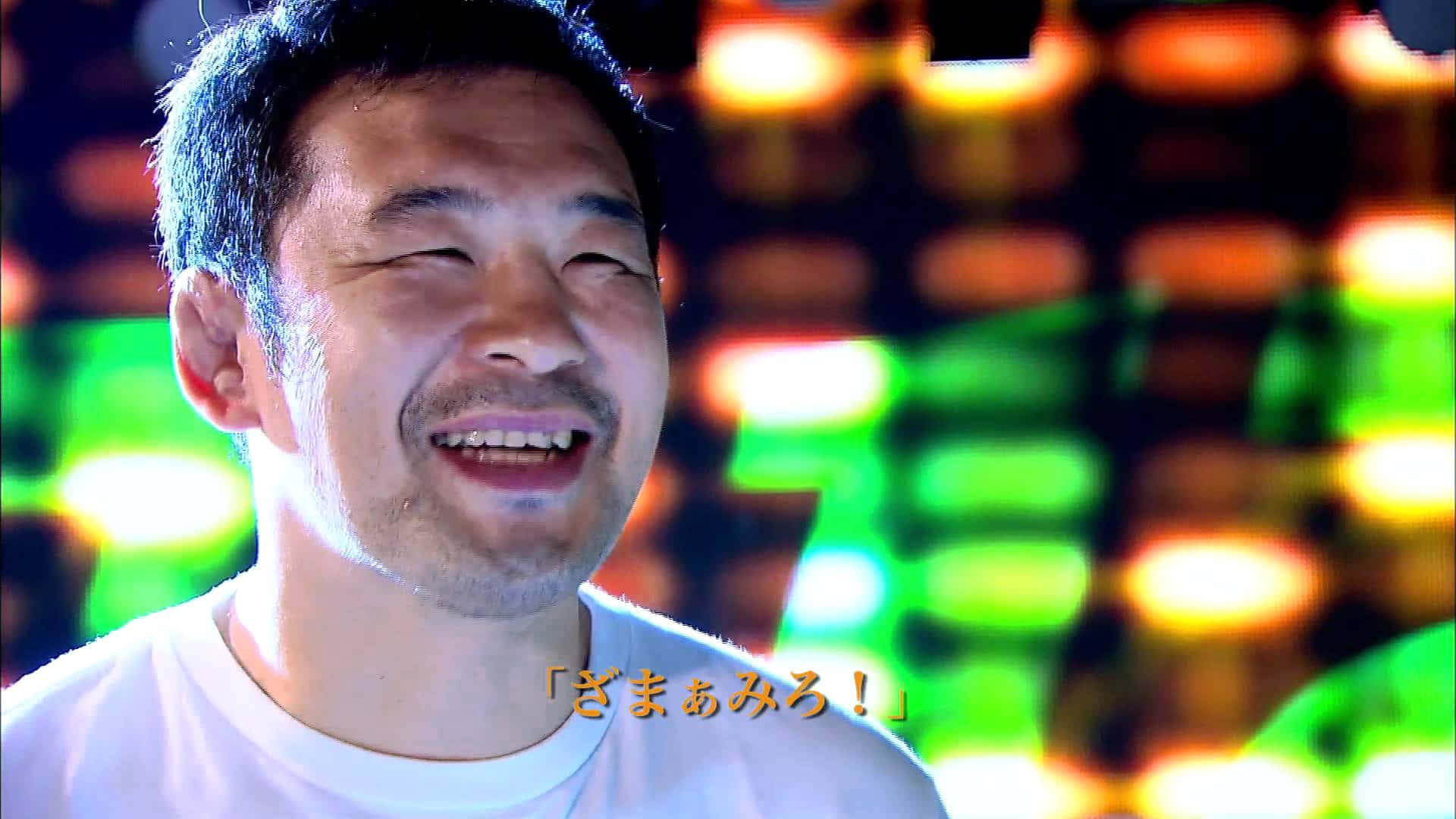 日本職業摔角手櫻庭和志接受訪問 壁紙 — 一個男人在充滿活力的模糊背景中，對著發光的霓虹燈快樂地大笑。