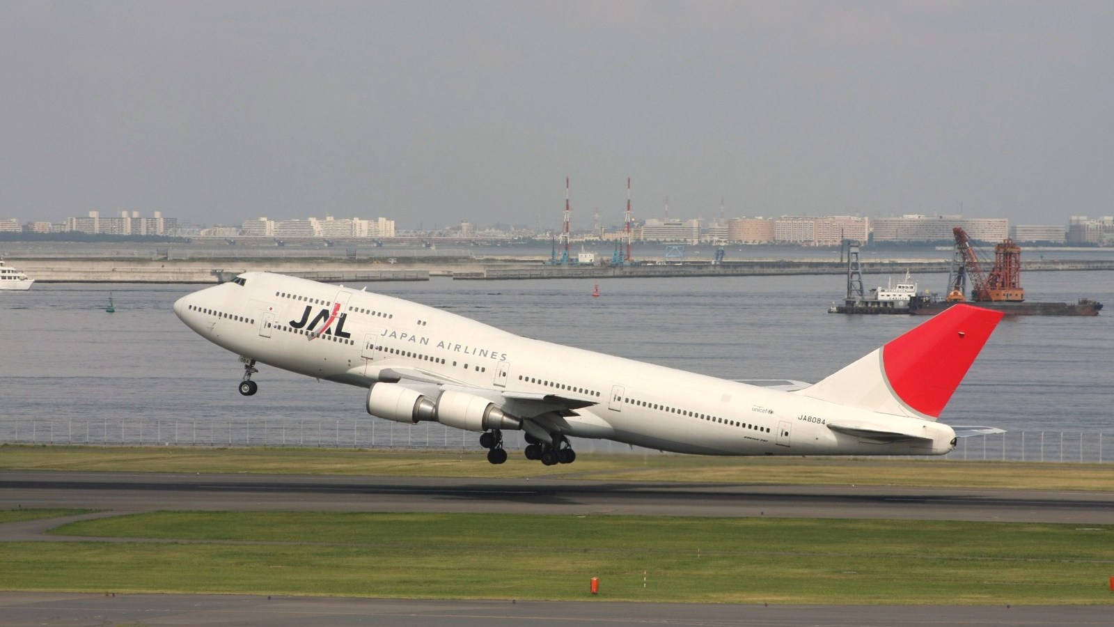 日本航空飛機從海濱附近的跑道起飛，背景是城市天際線。