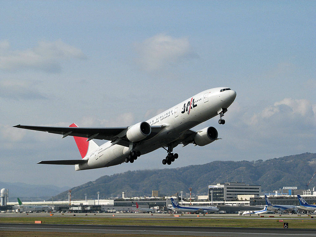 日本航空飛機從機場跑道起飛，背景有山脈。