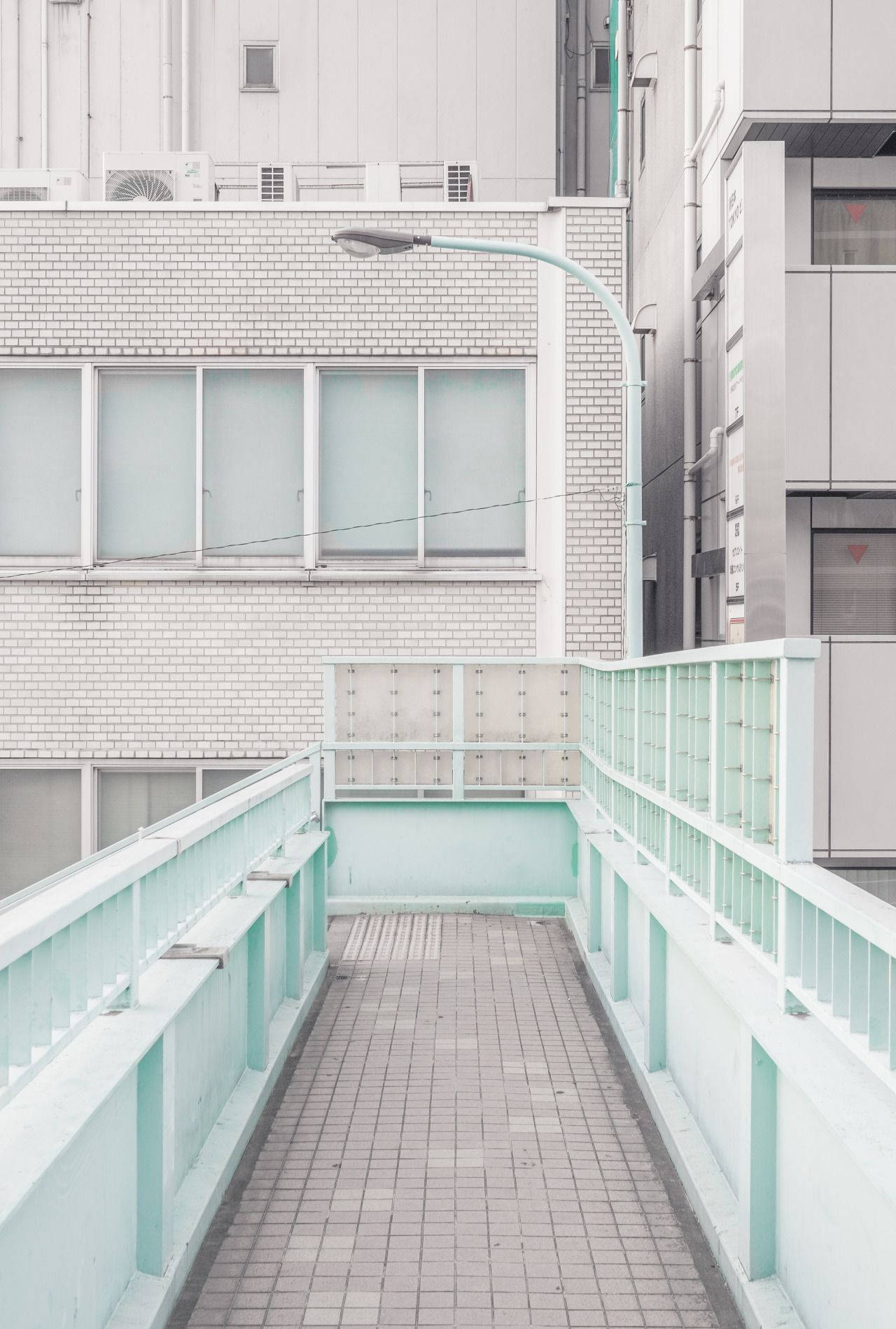 純白美學Tumblr日本行人橋 壁紙 — 一條狹窄的薄荷綠色行人天橋，舖有瓷磚地板，在柔和日光下連接現代都市建築之間。