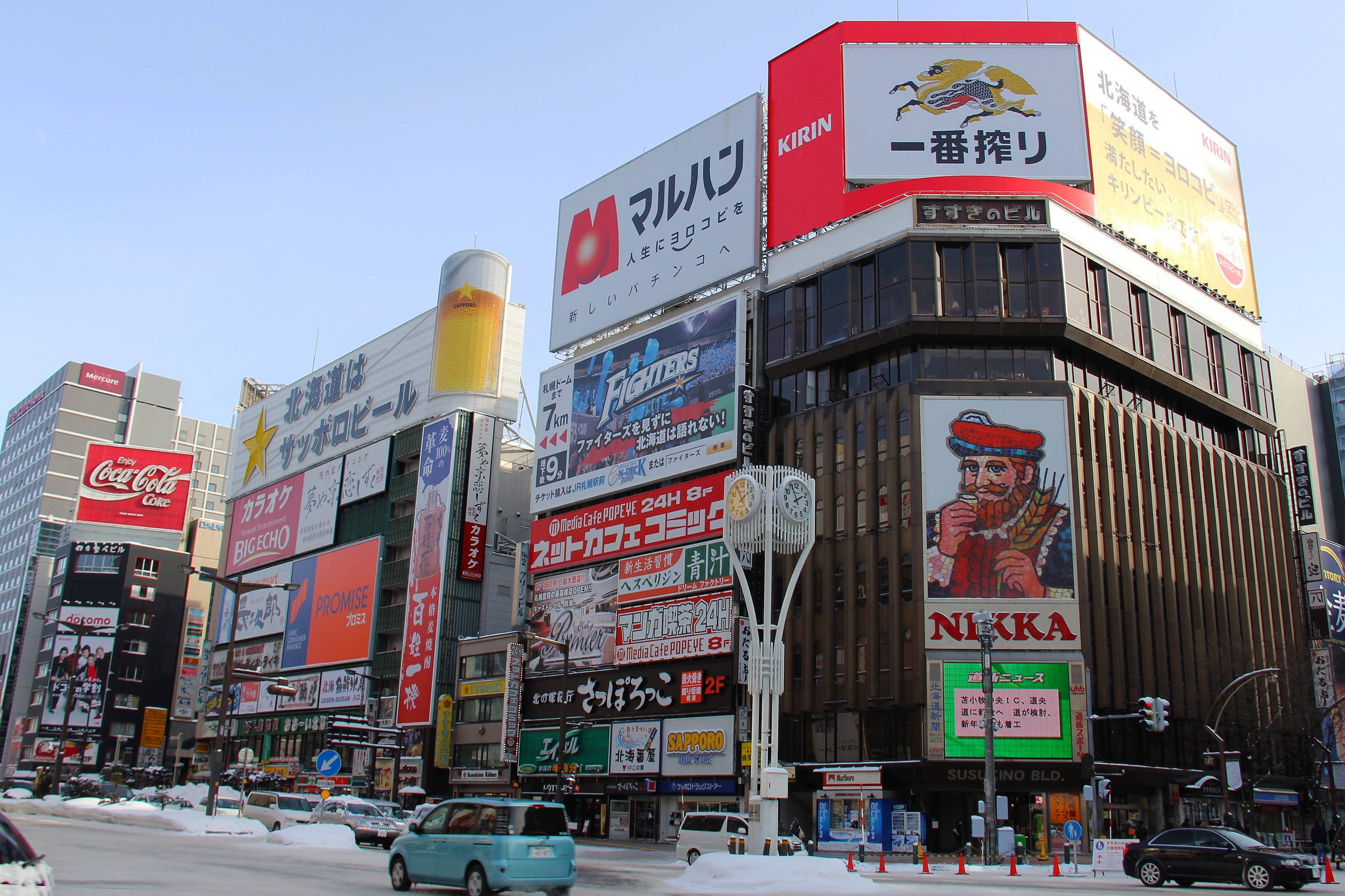 日本購物廣場 壁紙 — 白雪覆蓋著一條繁華的日本城市街道，兩旁是高聳的建築物，上面掛滿了色彩繽紛的霓虹招牌和廣告，在清澈的藍天下。