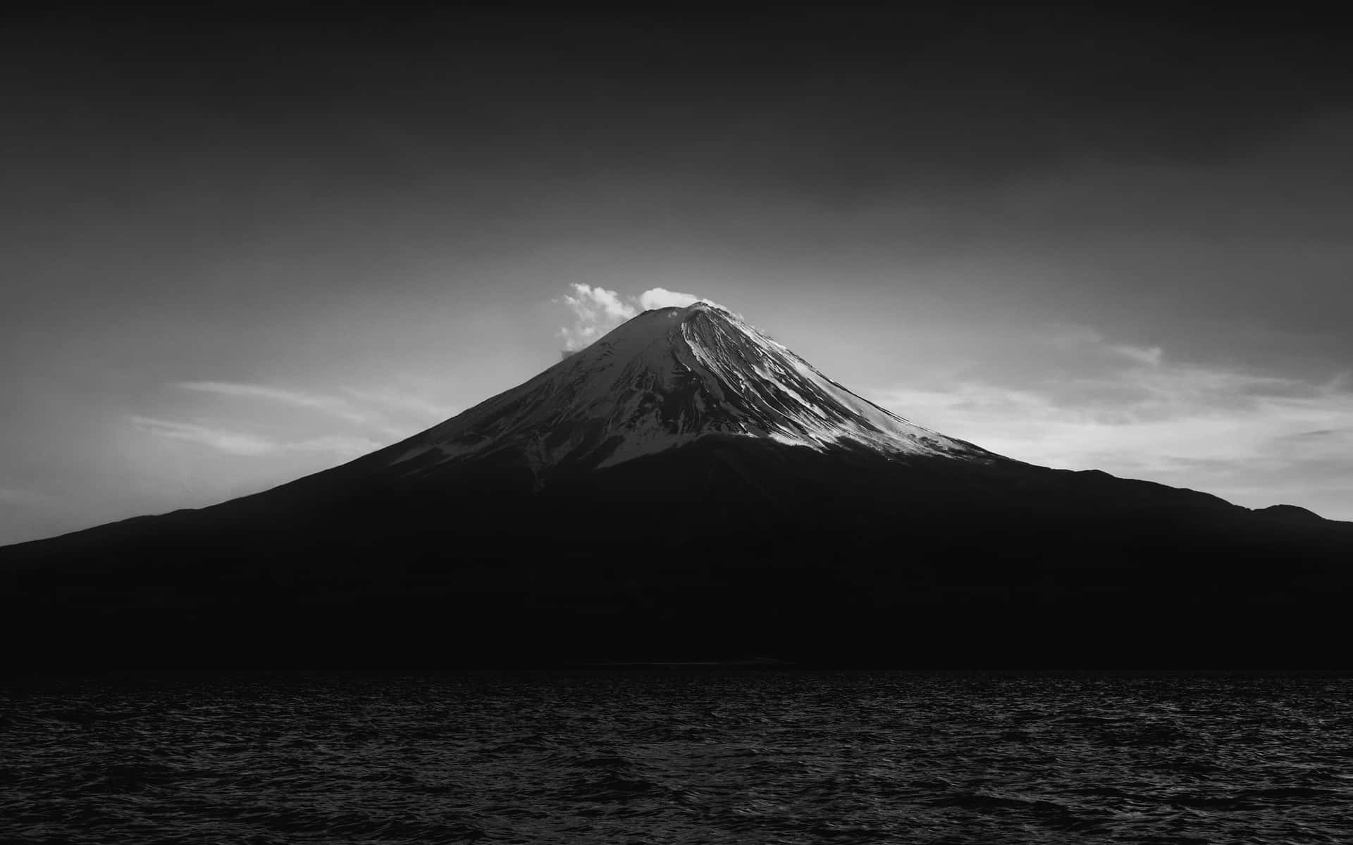 多雲天空下，黑暗湖泊上方的雪山輪廓。