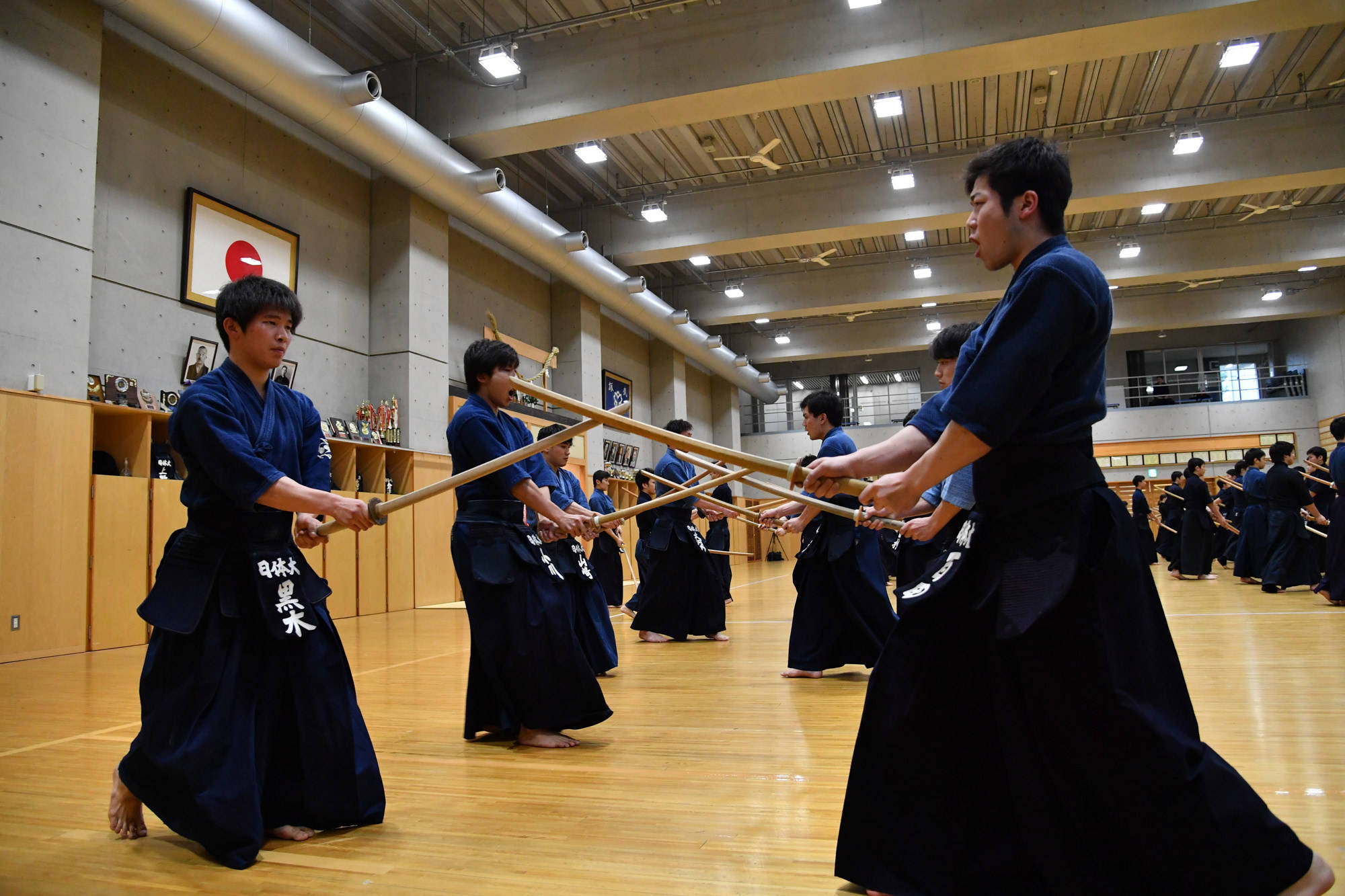 日本體育教育大學劍道社學生 壁紙 — 身穿深藍色制服嘅年輕武術家喺明亮嘅木製道場用竹劍練習劍道。