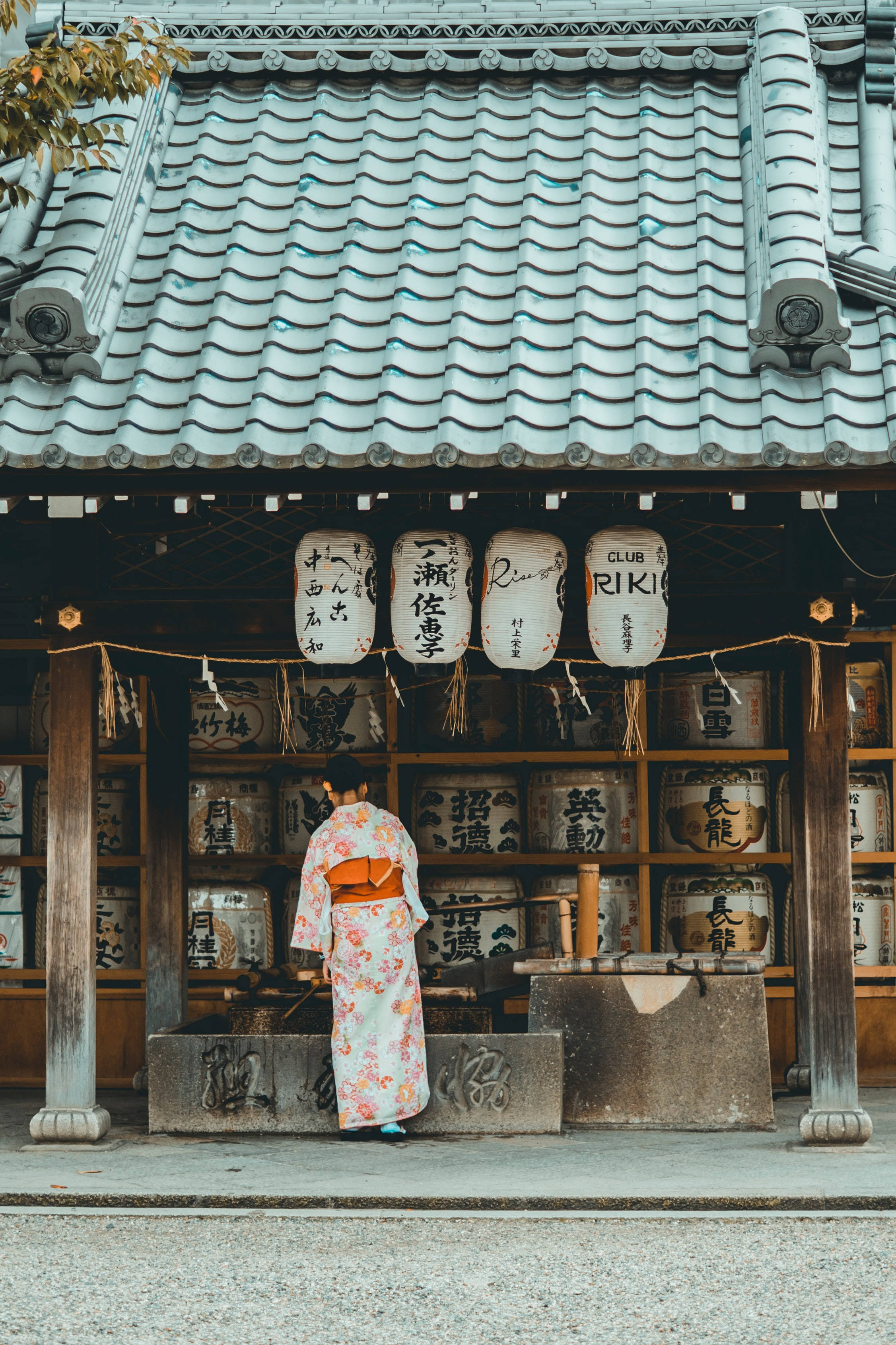 日本高清和服少女 壁紙 — 一位穿著花卉和服的人站在傳統日本神社前，神社有瓦片屋頂和懸掛的燈籠。