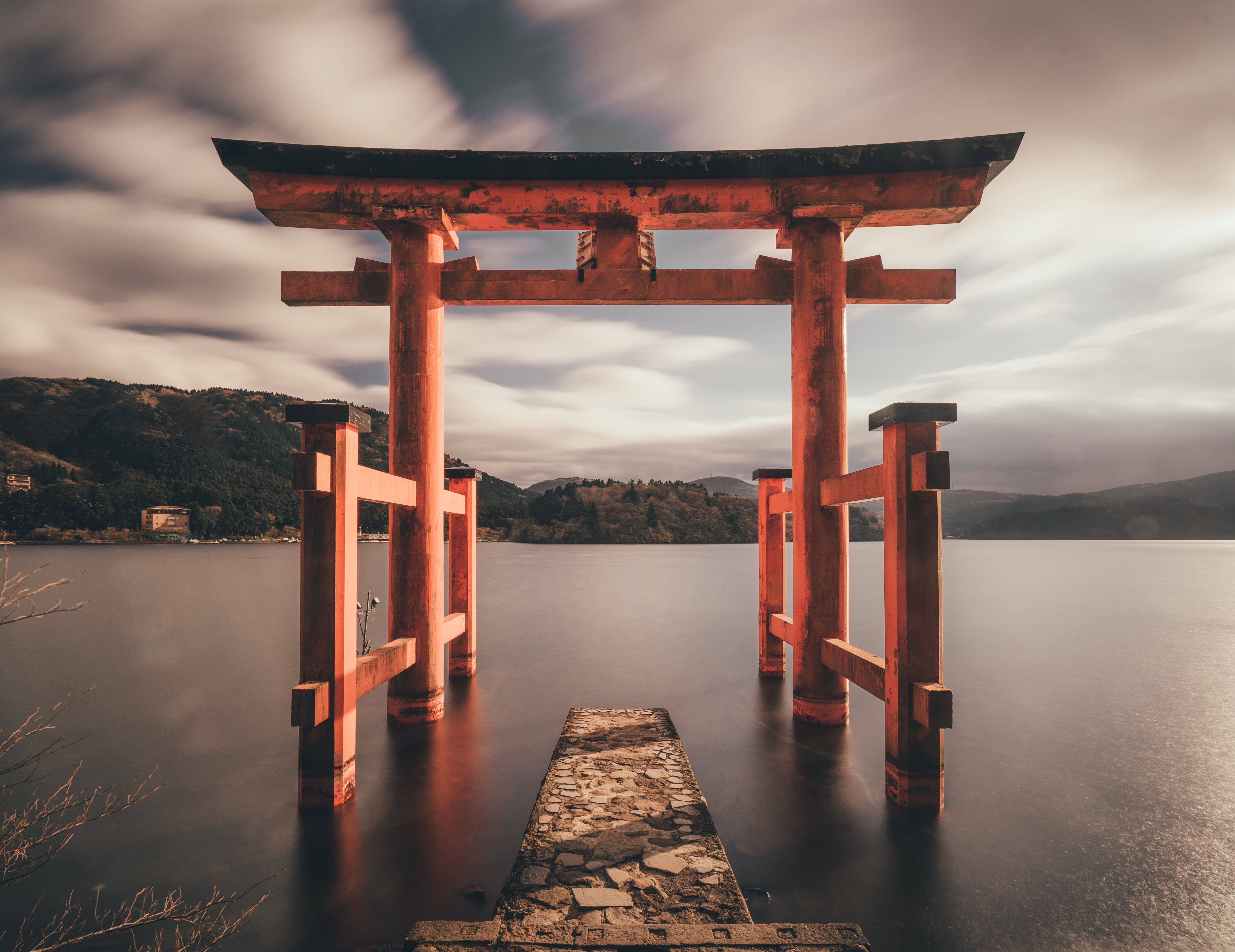 夕陽下，水中紅色鳥居與石徑，背景是山巒。