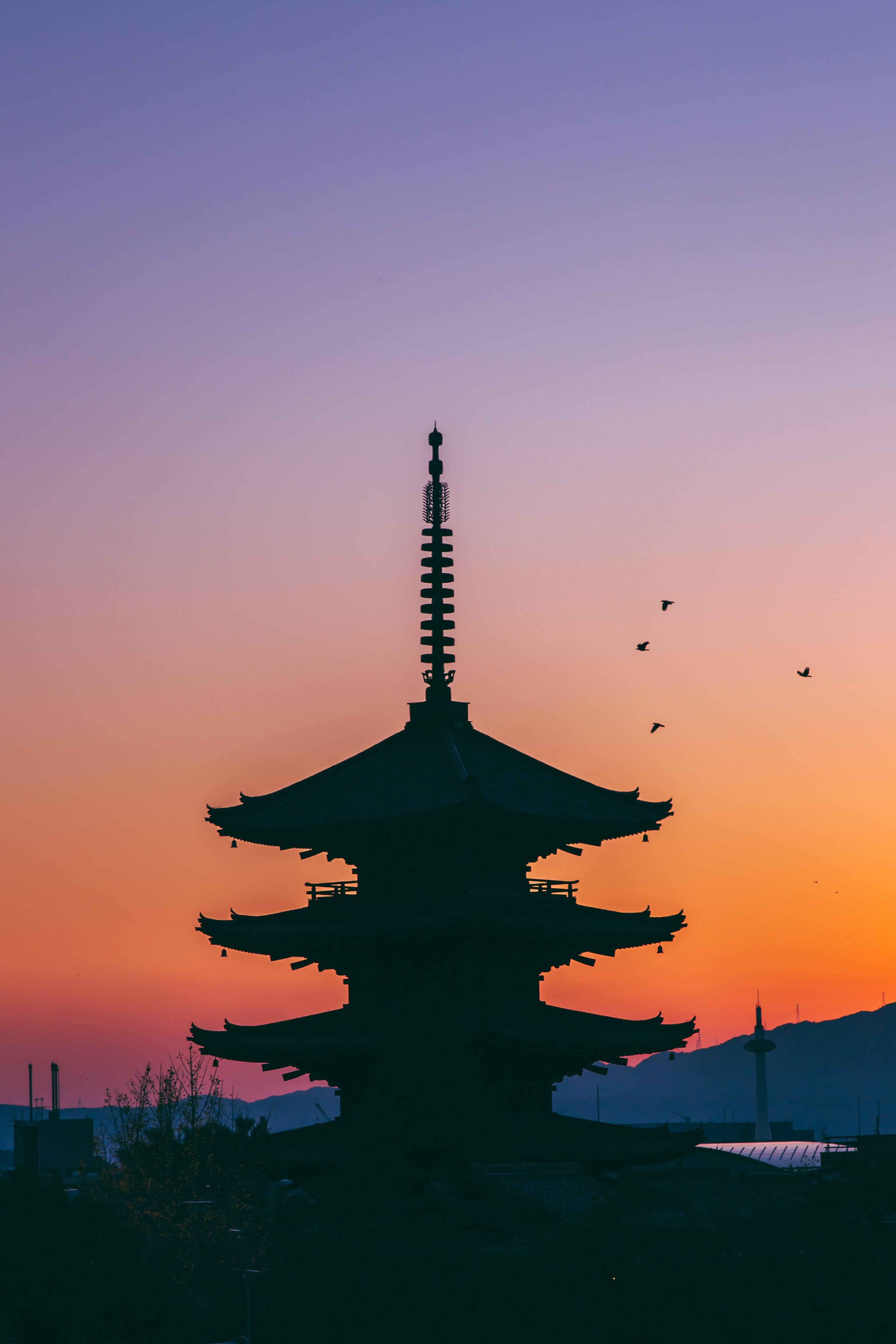 日落時分的寶塔剪影，鳥兒在橙色和紫色天空中飛翔