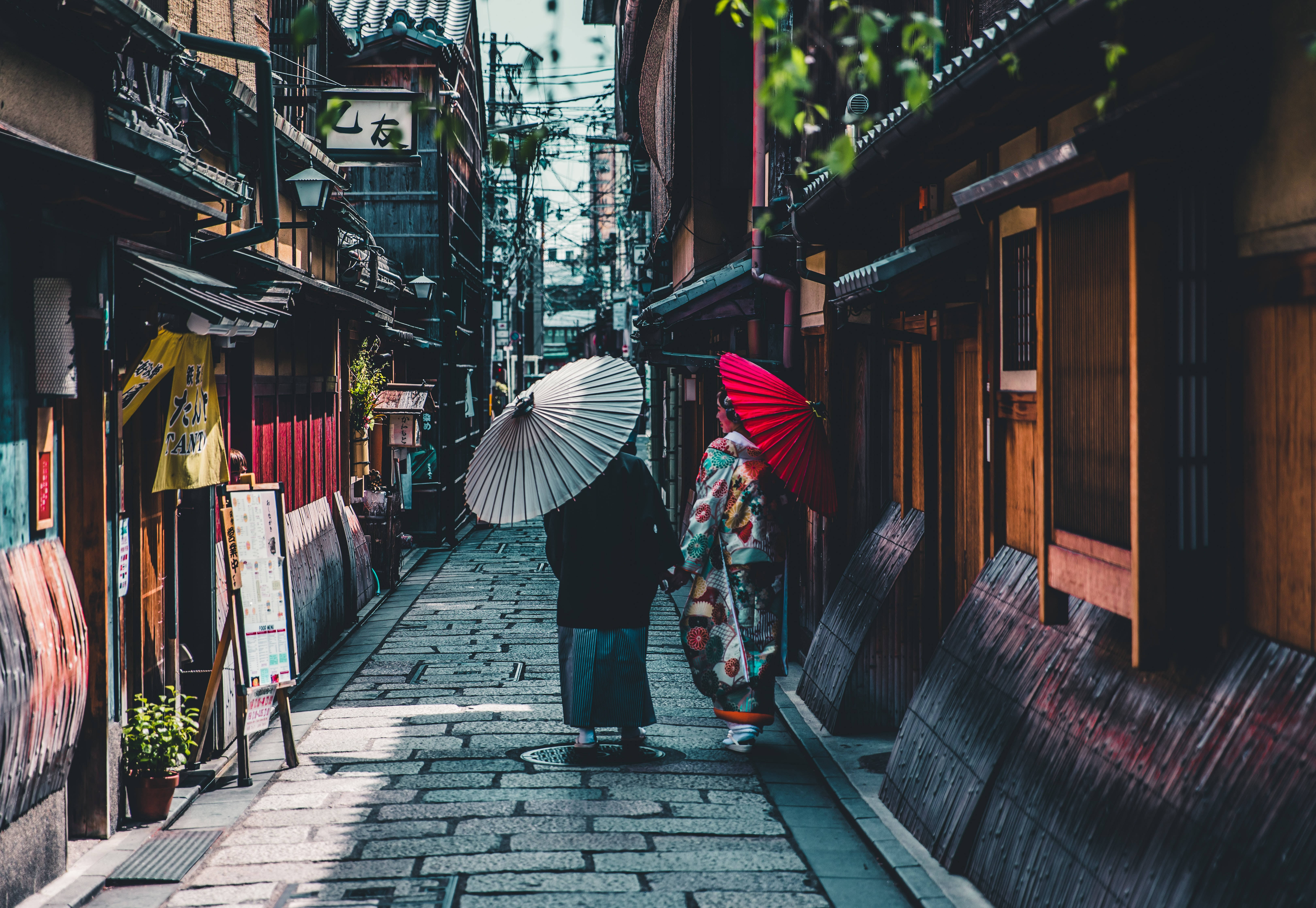 兩個穿著傳統日本服裝的人沿著一條狹窄的石頭小巷行走。