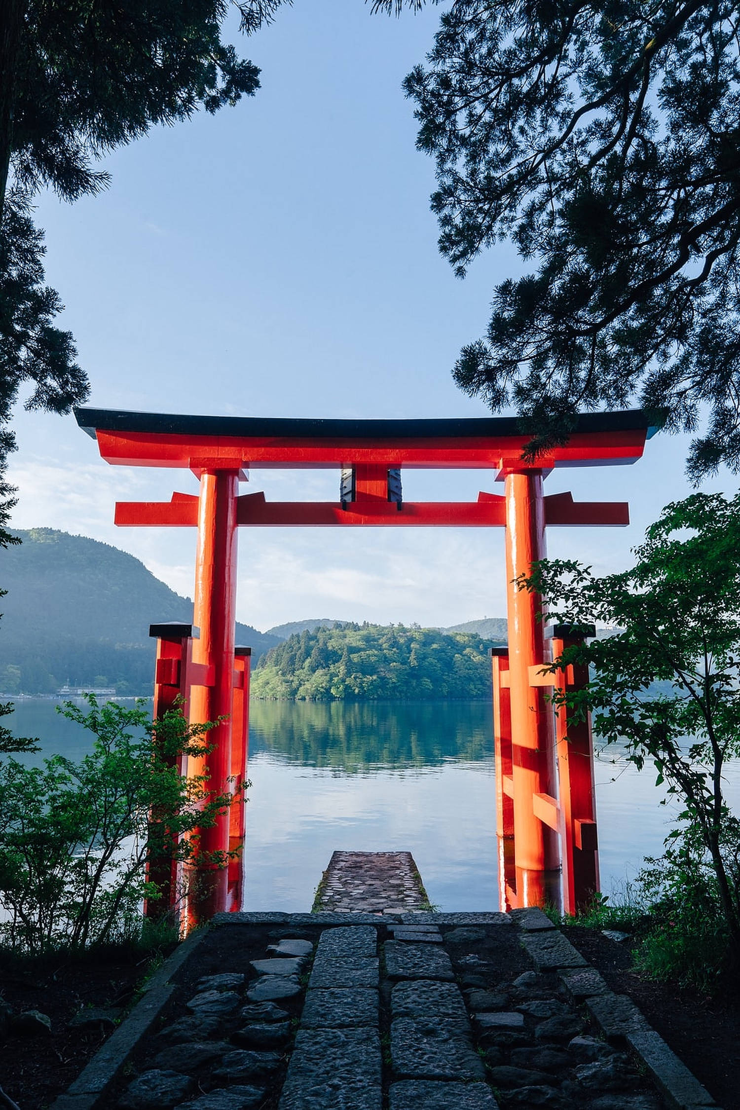 日本鳥居門 壁紙 — 一座鮮紅色的鳥居矗立在寧靜的湖邊，四周綠樹成蔭，天空湛藍。