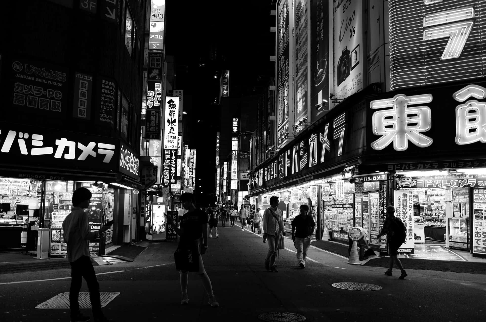 夜晚東京擁擠街道的黑白照片，有發光的招牌和行人。