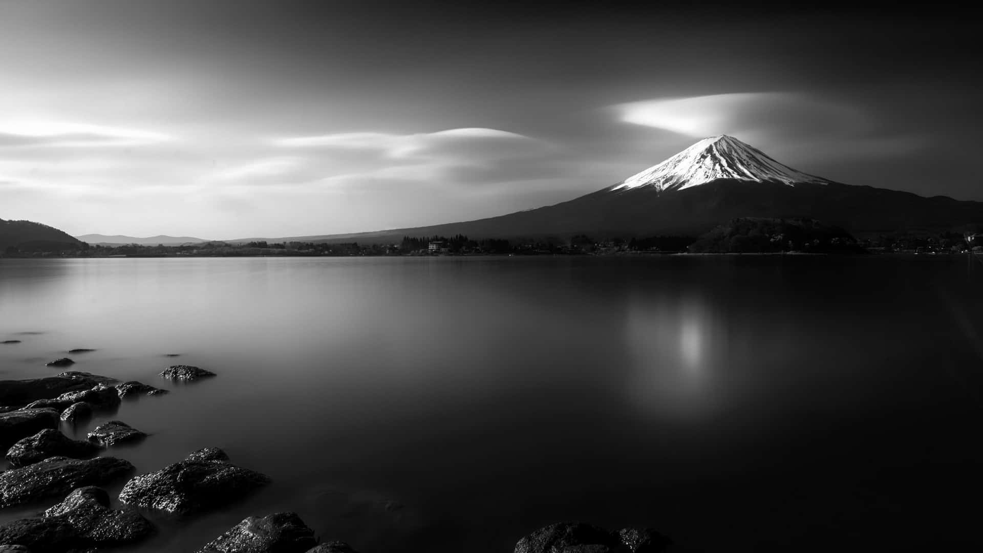 富士山在戲劇性雲層下的平靜湖泊倒影，黑白照片。