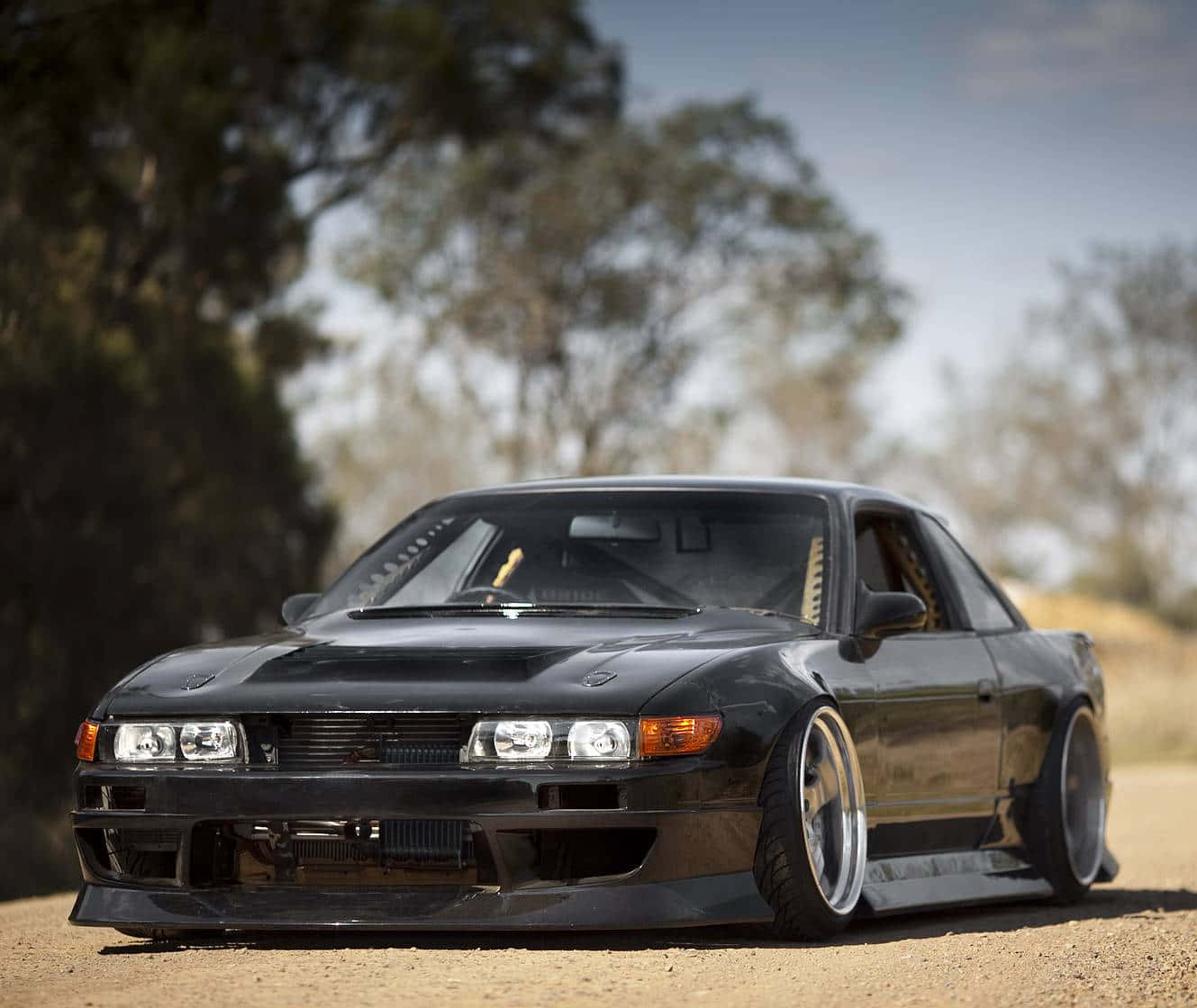 黑色改裝日產Skyline GT-R停放在泥路上，背景有樹木。