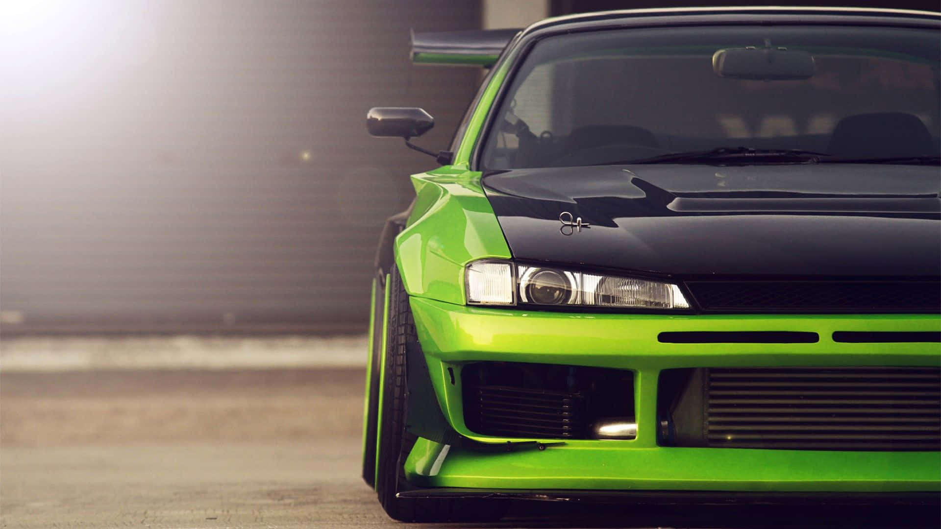 日產Silvia S15 定製款 壁紙 — 一輛鮮豔的青檸綠色和黑色改裝跑車，帶有大型後擾流板，在日出時停放在倉庫前。