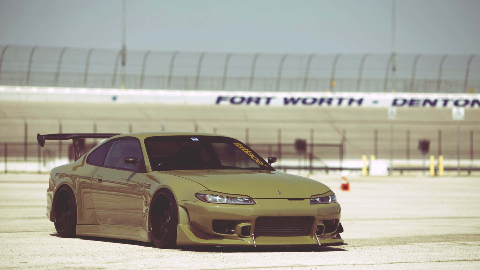 日產Silvia S15 端港區 壁紙 — 一架金色改裝跑車配備大型尾翼，在煙霞籠罩的天空下停泊在賽車場上。