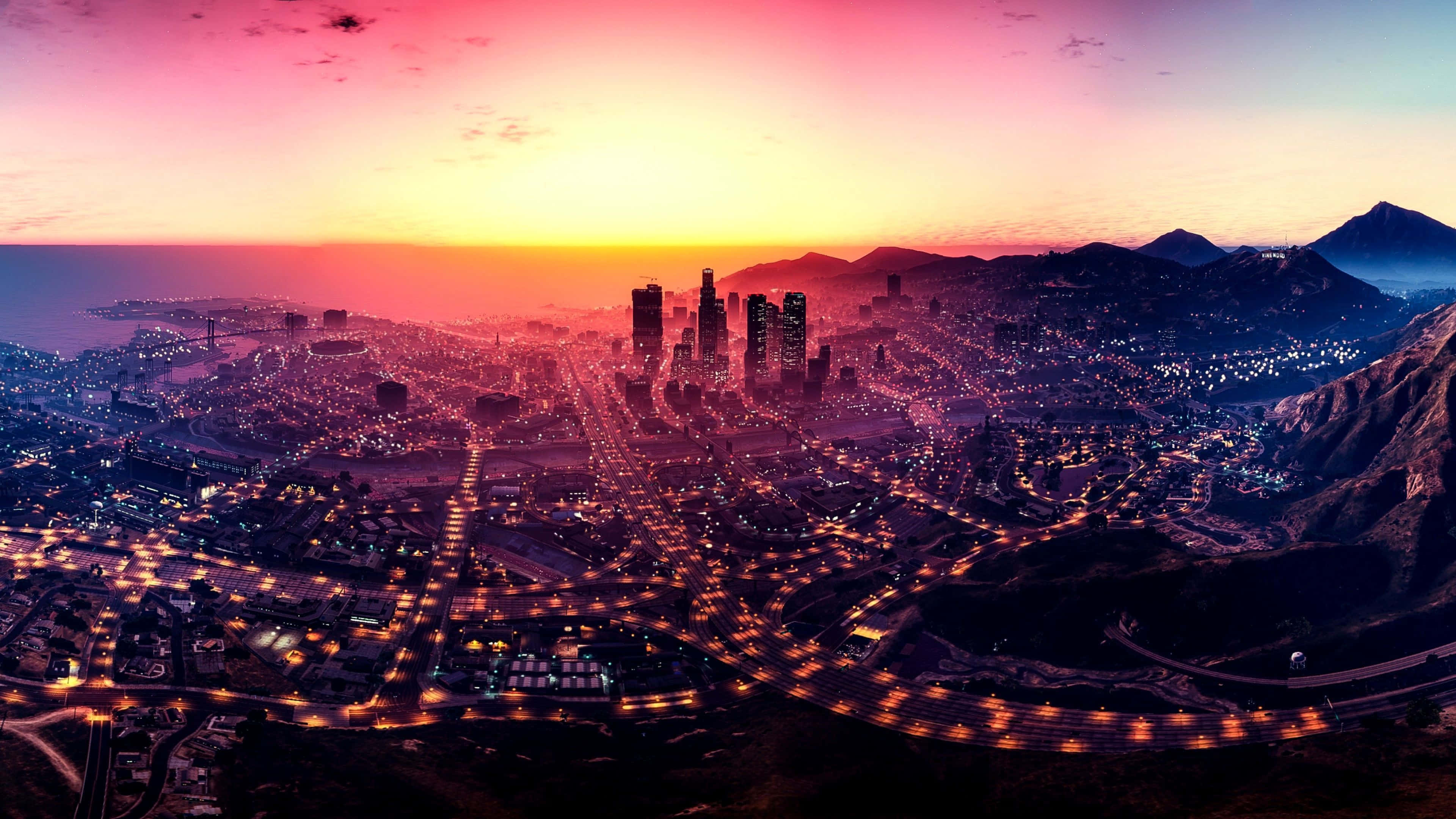 Gta 5 4K 桌布 壁紙 — 日落時分，一座廣闊城市的鳥瞰圖，發光的街道和摩天大樓映襯著充滿活力的粉紅色和橙色天空。