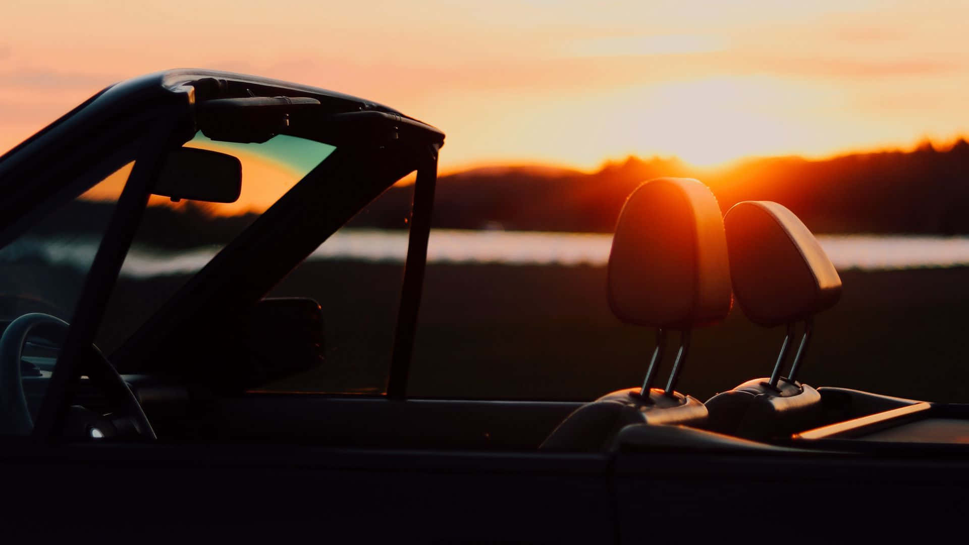 Sunset Drive 桌布 壁紙 — 日落時分，一輛開篷車的剪影，伴隨發光的橙色天空和遠處的水面。