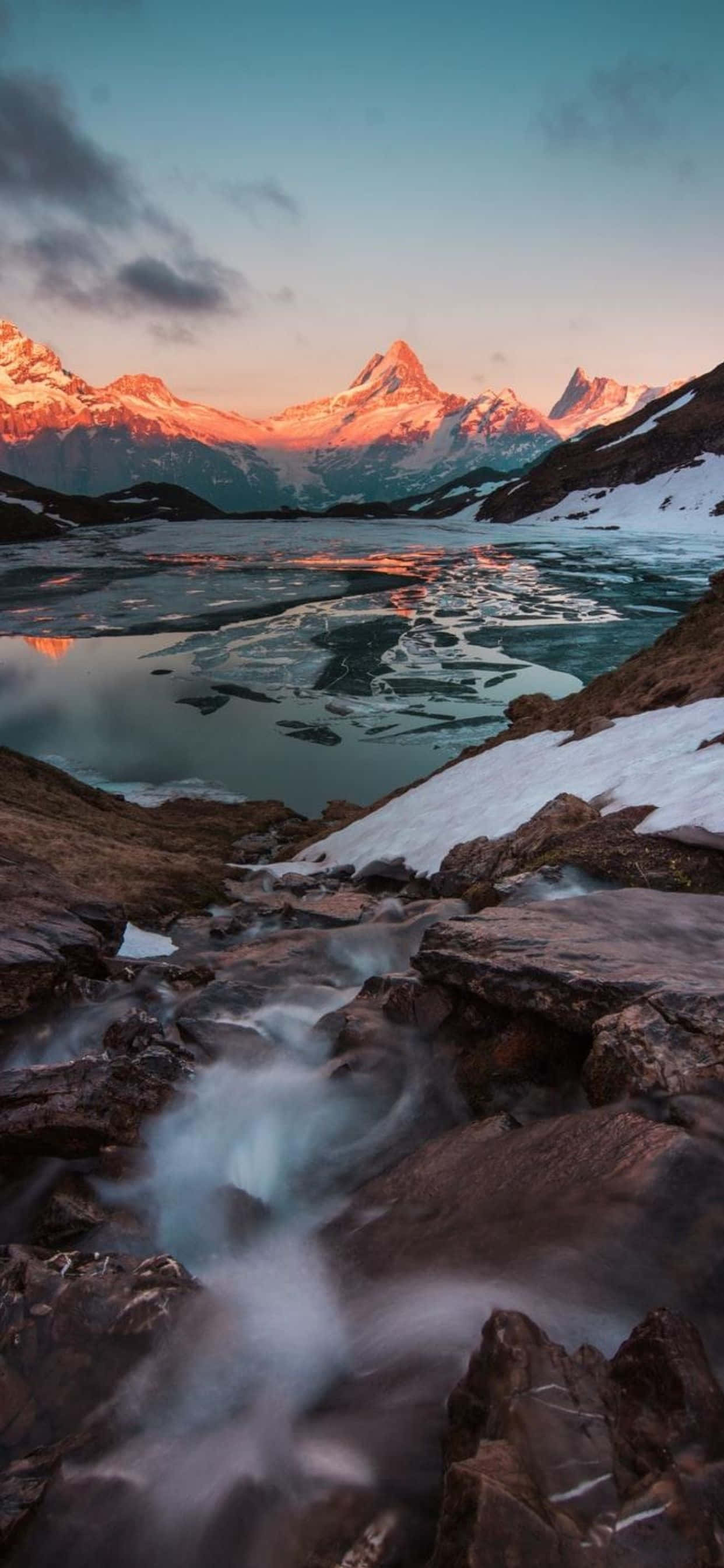 iPhone Xs Max 桌布 壁紙 — 日落時分，寧靜的高山湖泊倒映著積雪的山峰，前景中湍急的溪流流過岩石。