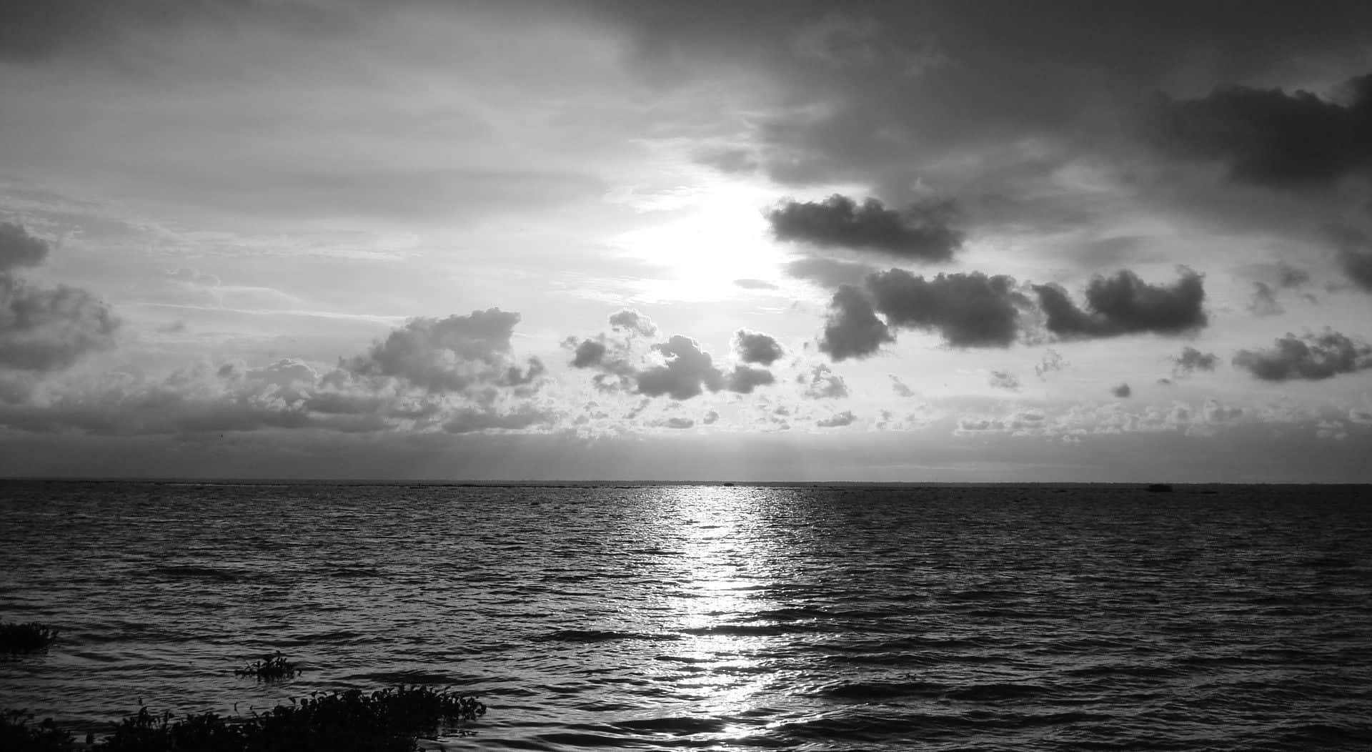 Black And White Ocean 桌布 壁紙 — 日落時分，寧靜的黑白海景，陽光穿過散落的雲層，反射在漣漪的水面上。