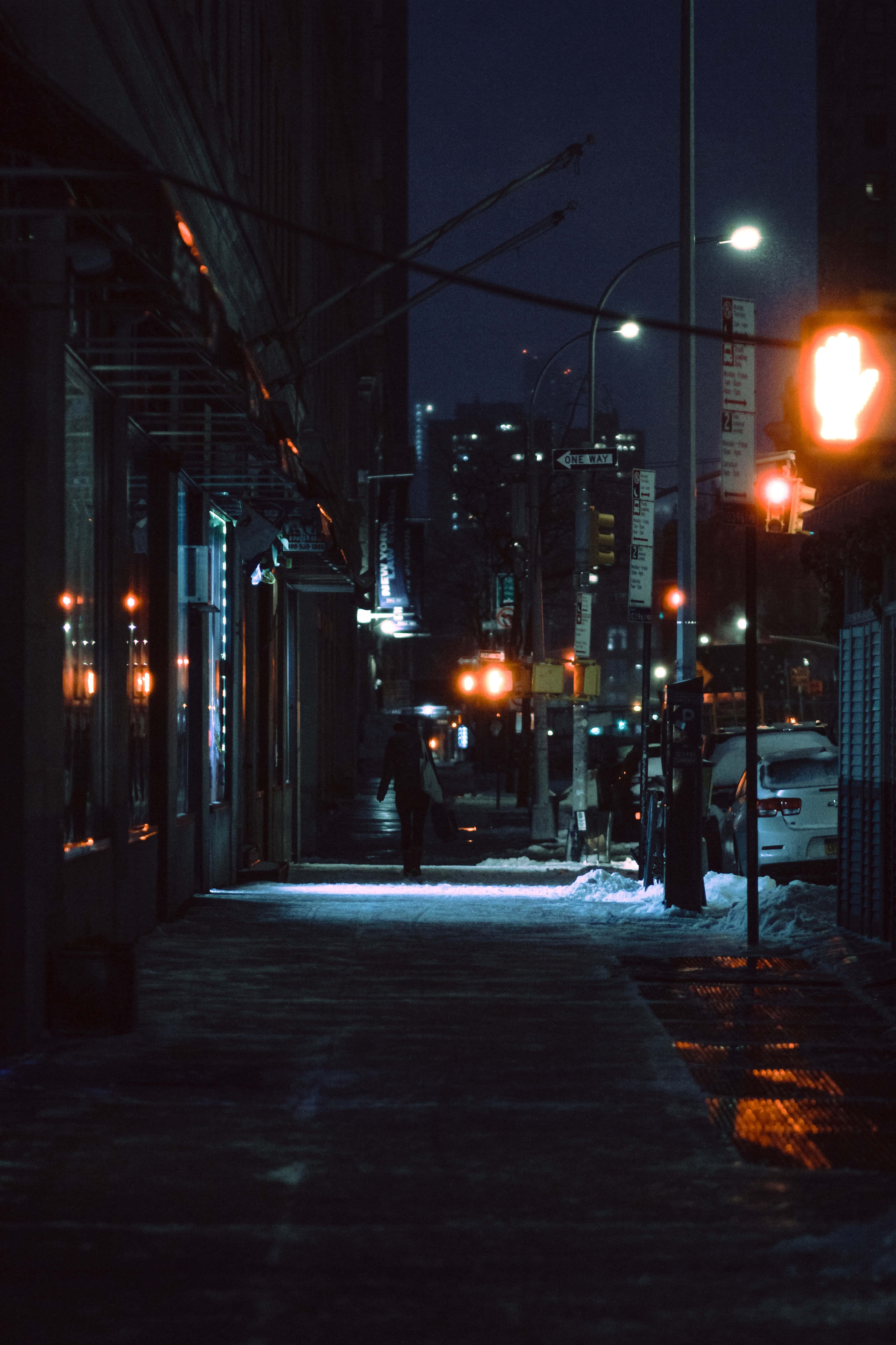 日落時分，星空漸次綻放 壁紙 — 夜晚，一個孤獨的身影走在積雪的城市人行道上，被發光的紅色交通燈和路燈照亮。
